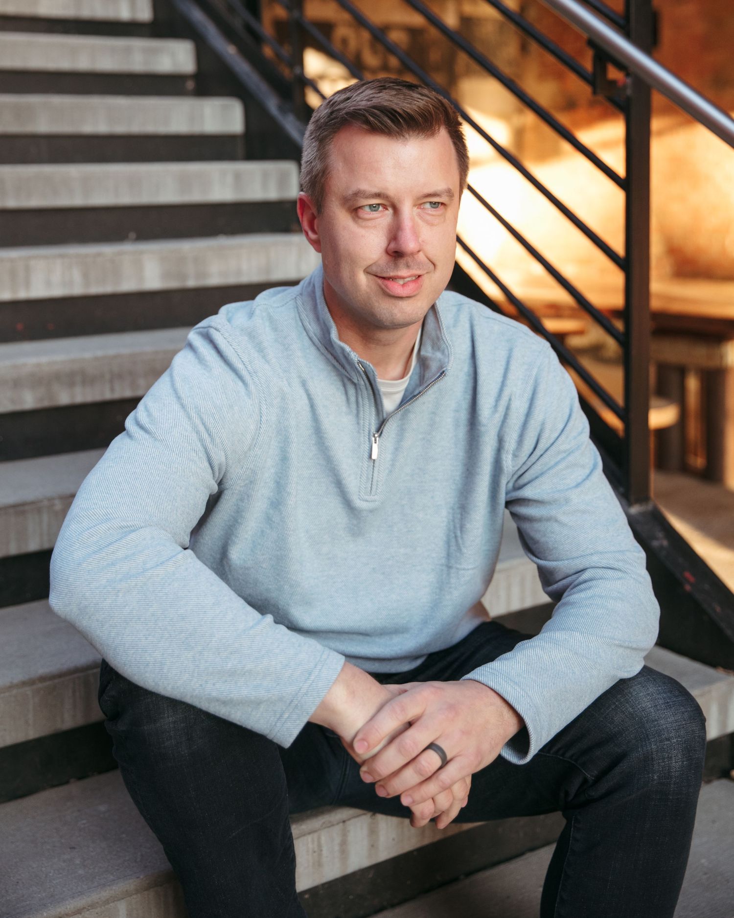 Individual in light gray sweater sitting on concrete stairs in industrial setting.