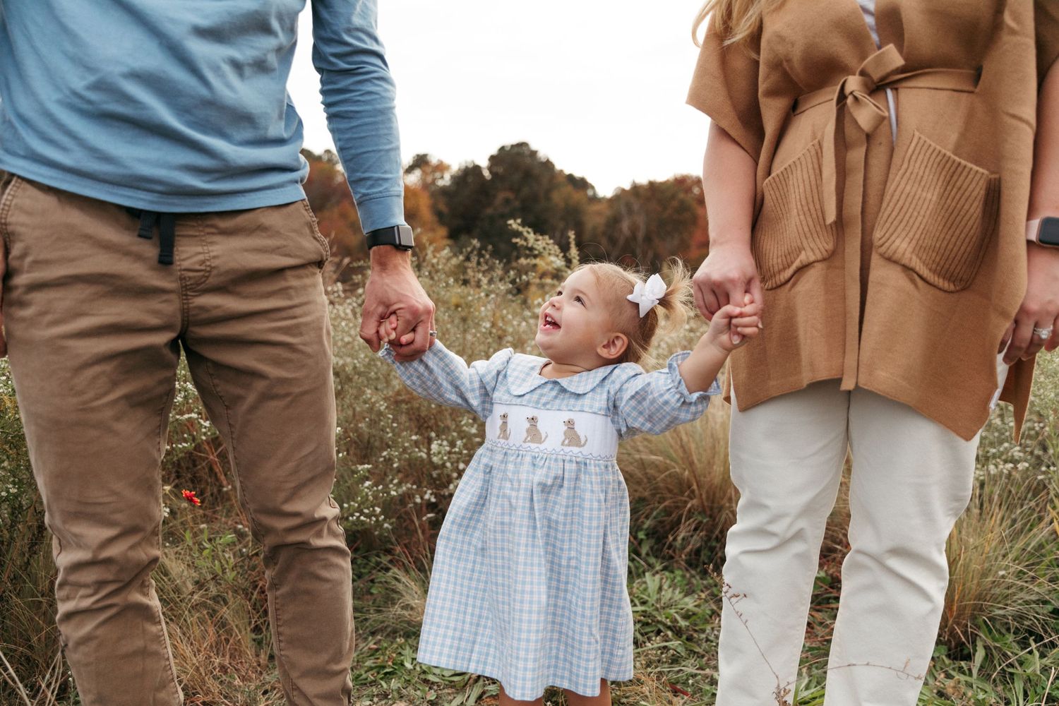 Low angle view of toddler holding hands with parents while walking in tall grass.