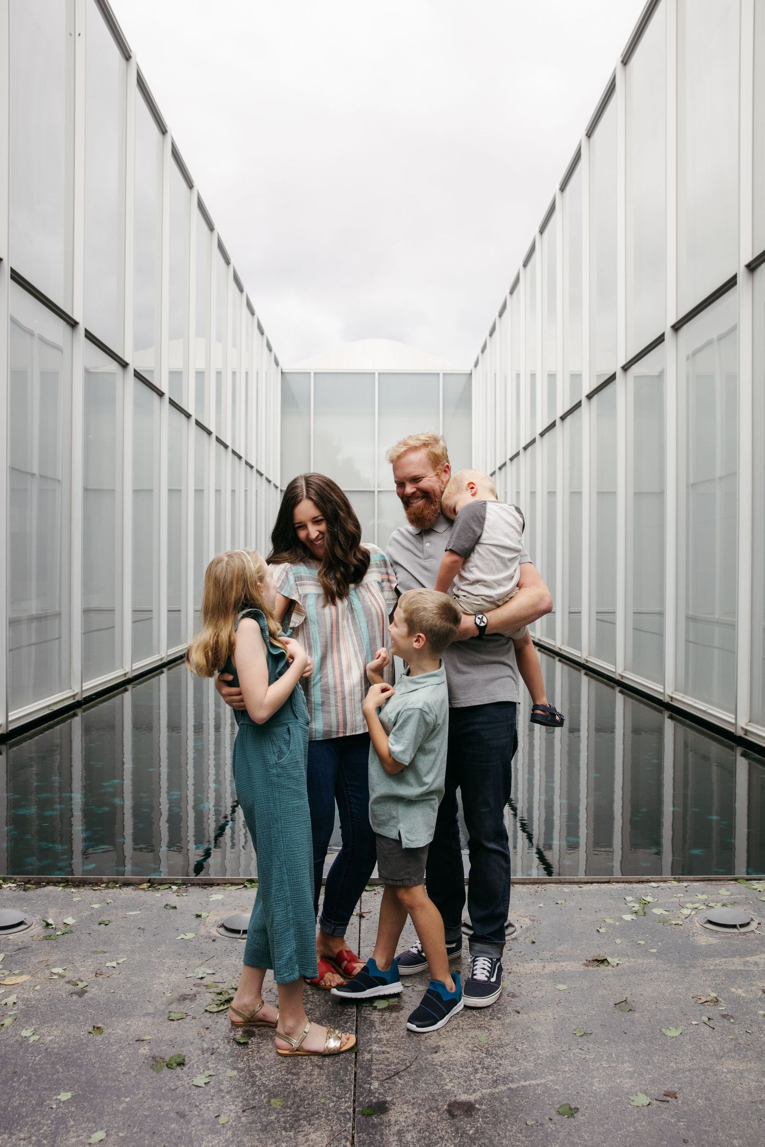Family shares playful moment in modern white corridor with geometric lines.