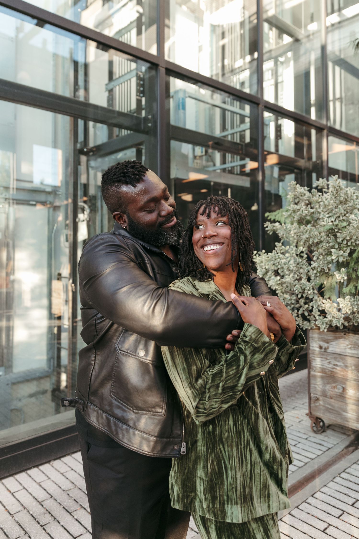 Affectionate couple embracing and laughing together outside a modern glass building.