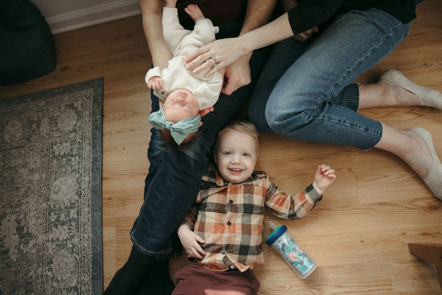 A joyful family scene on hardwood floors with a patterned rug in the background.