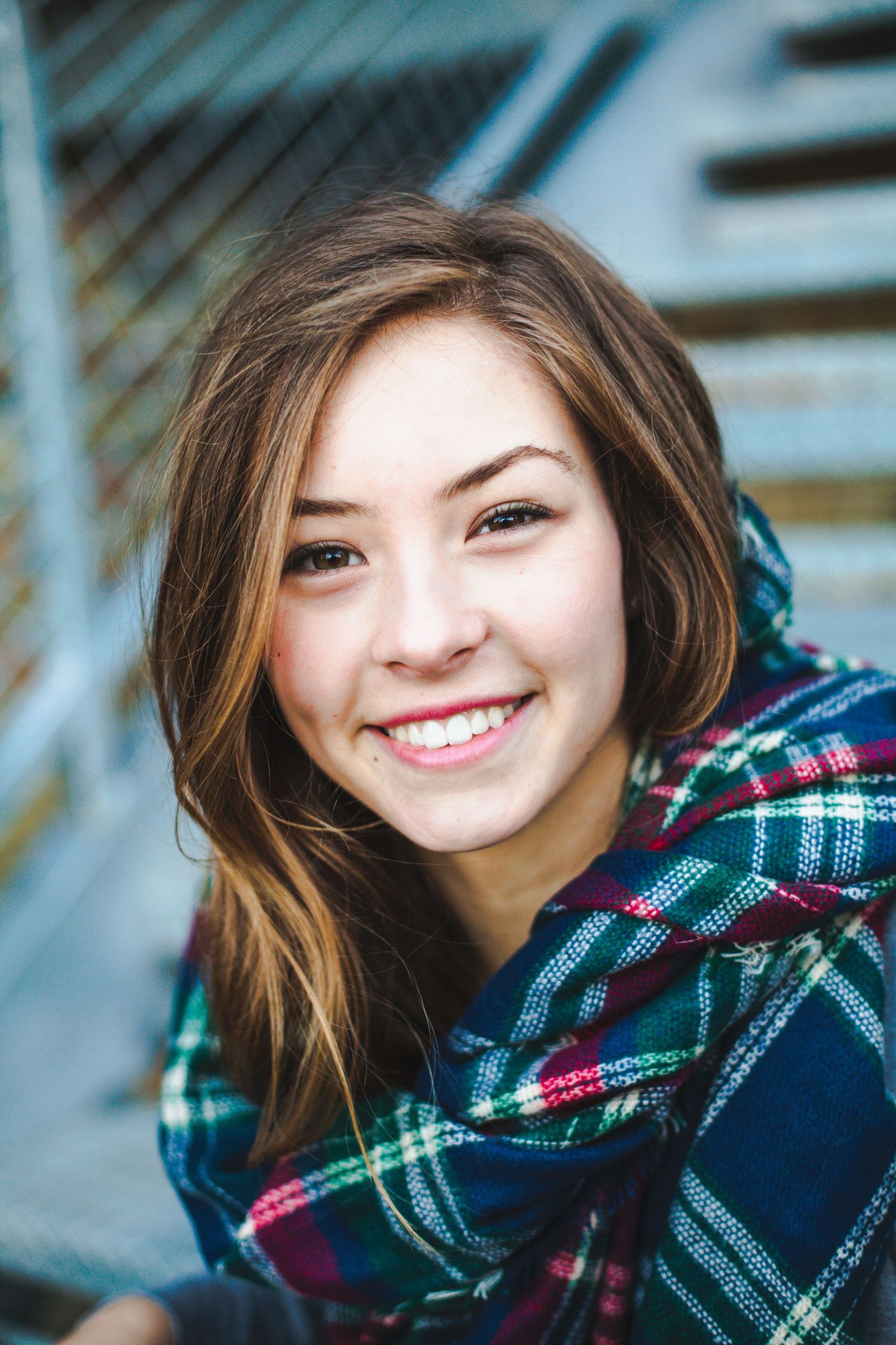 Close-up portrait featuring a warm smile and plaid scarf against a blurred background.