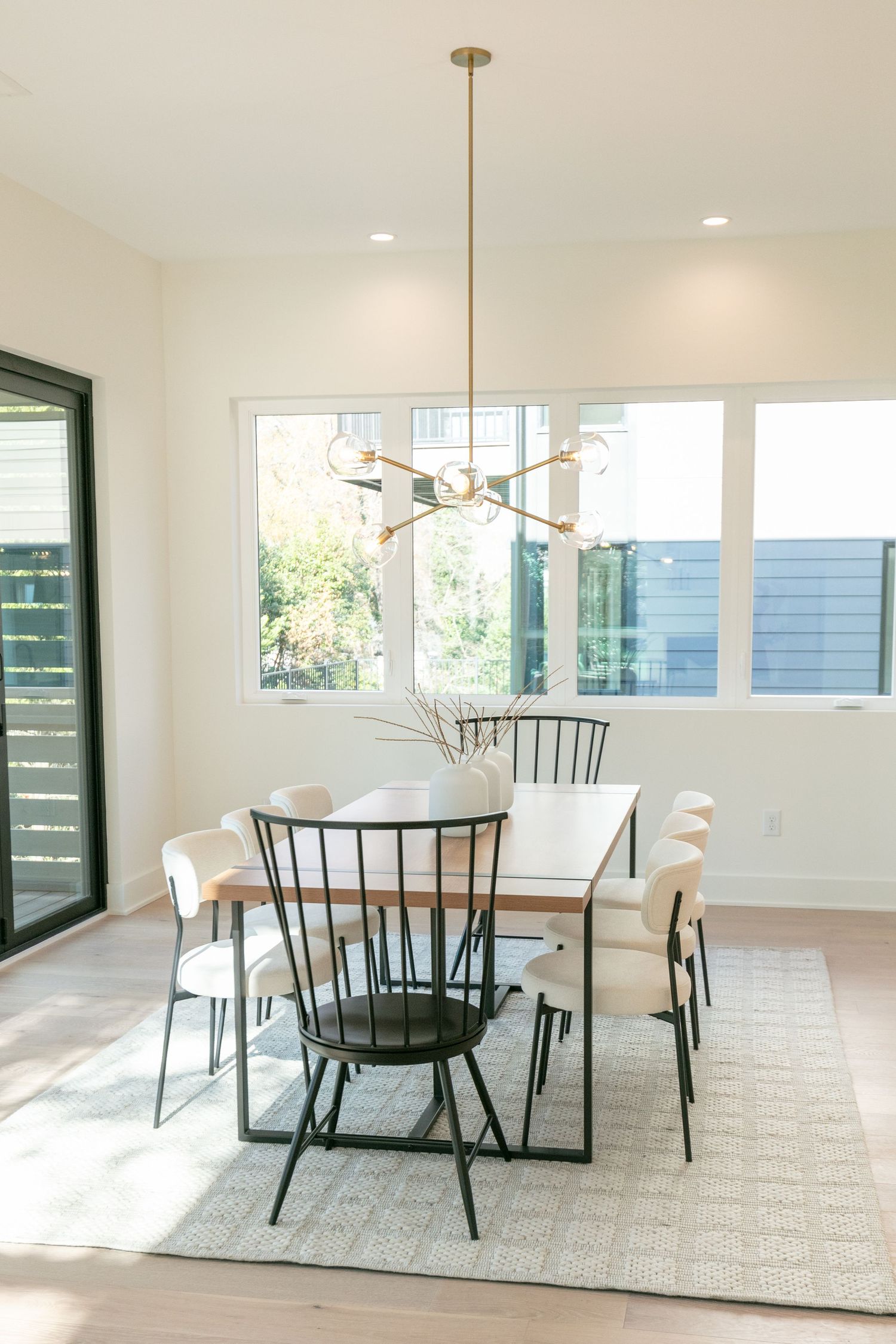 Modern dining area with white walls, black chairs, and pendant lighting illuminating a simple rectangular table on patterned rug.