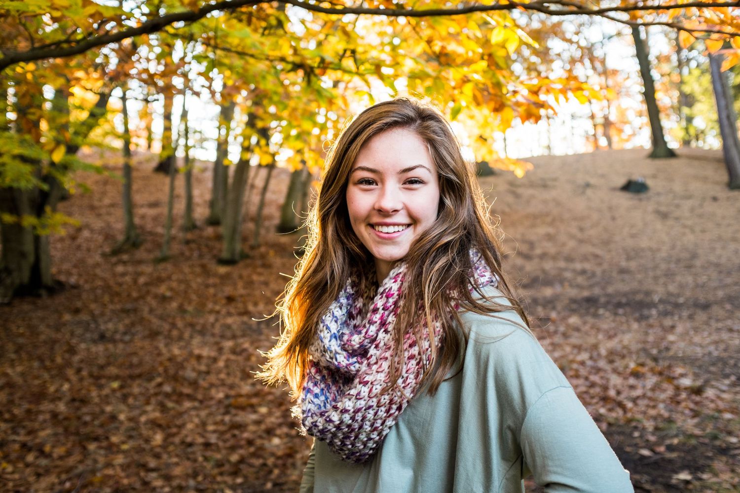 A casual autumn portrait with fall foliage in the background on a sunny day.