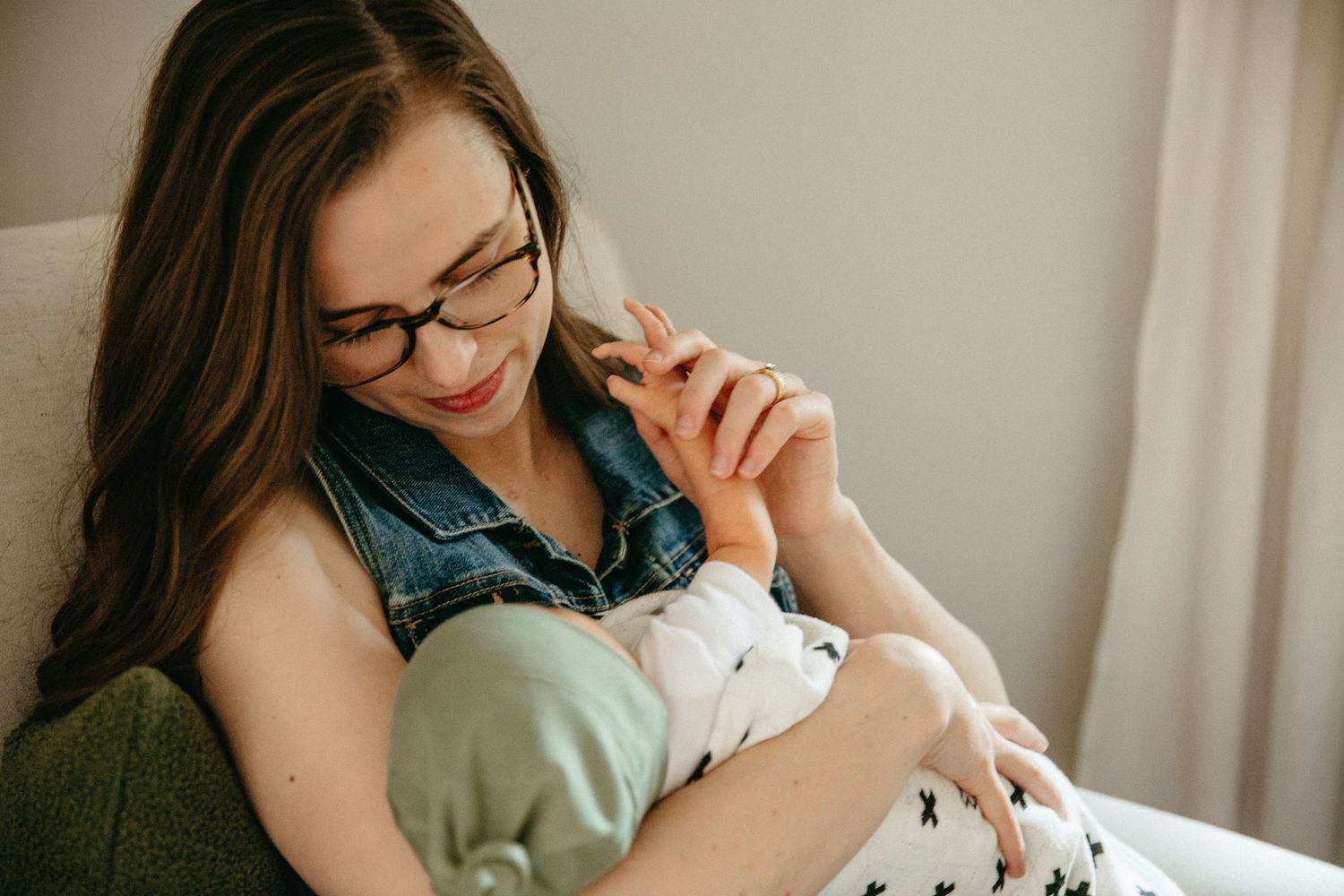 A parent wearing glasses holds and gazes at their sleeping baby.