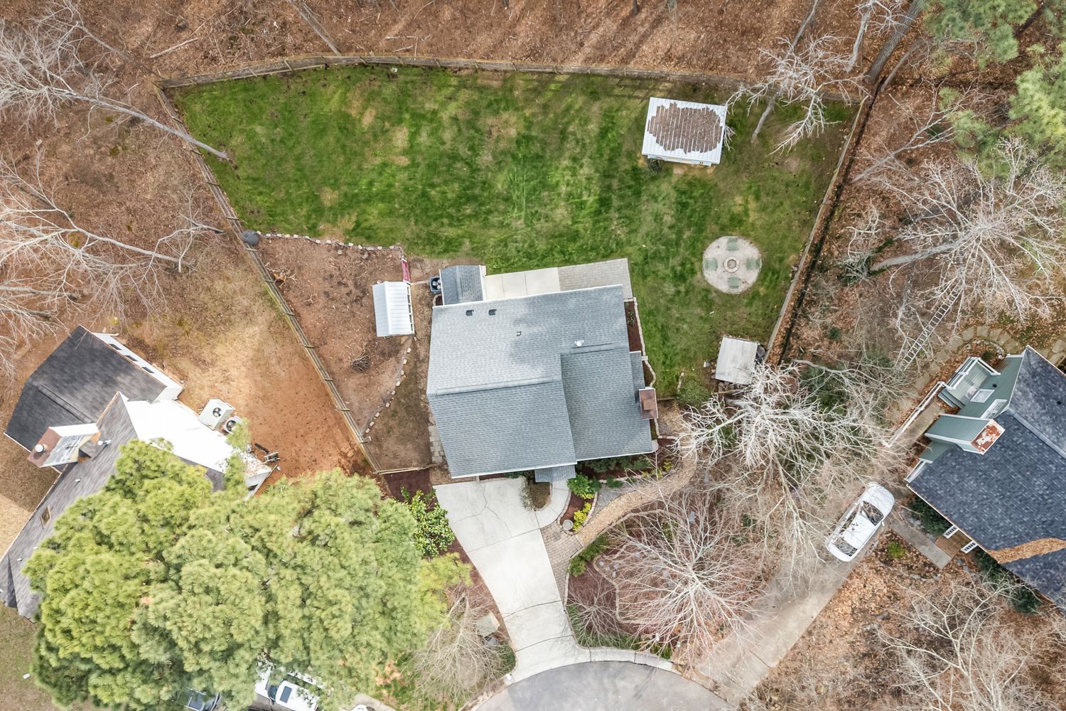 Aerial view of a residential home with gray roof, large green lawn, and surrounding trees in a suburban neighborhood.