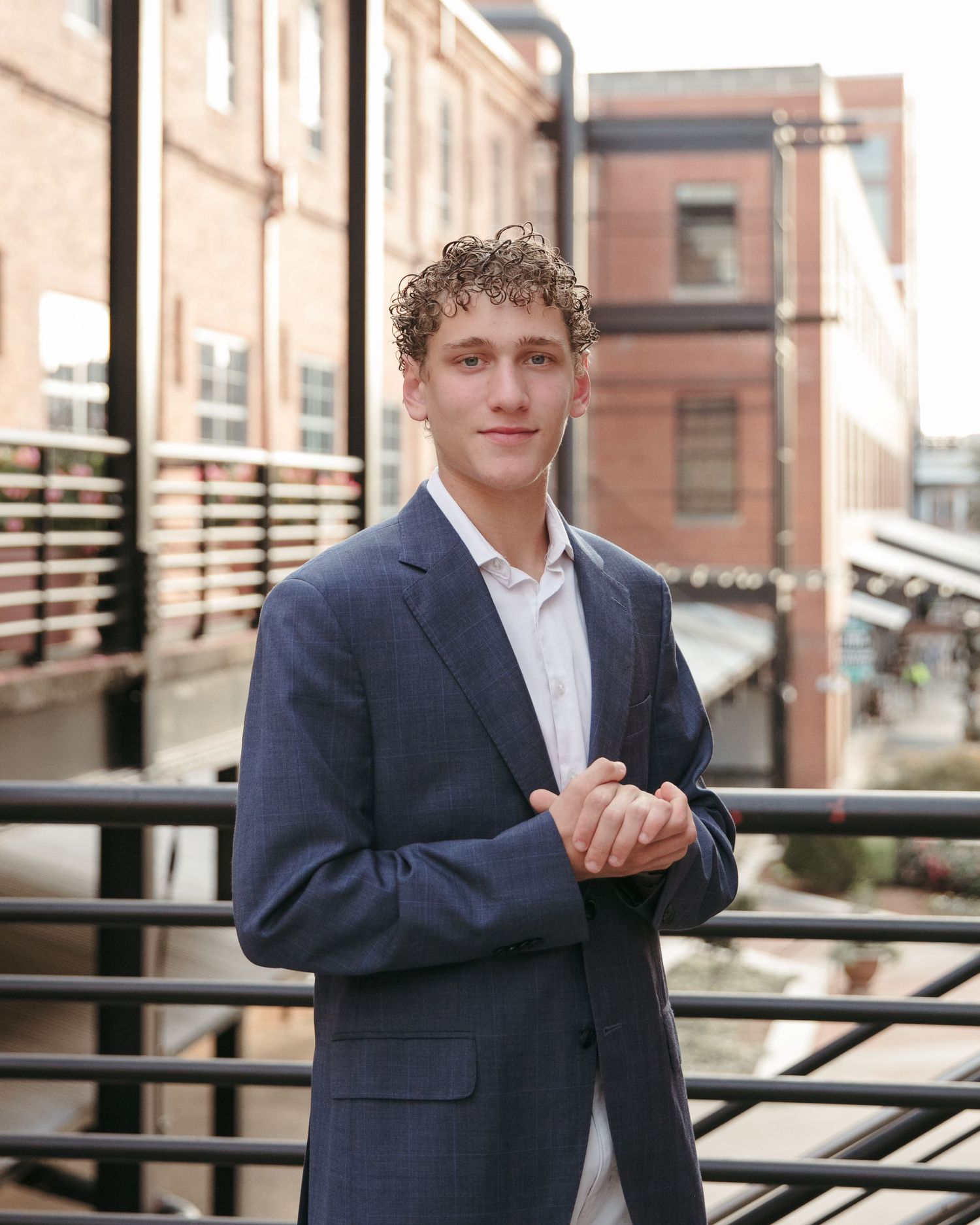 A professional portrait of someone in a navy blazer against an urban brick building backdrop.