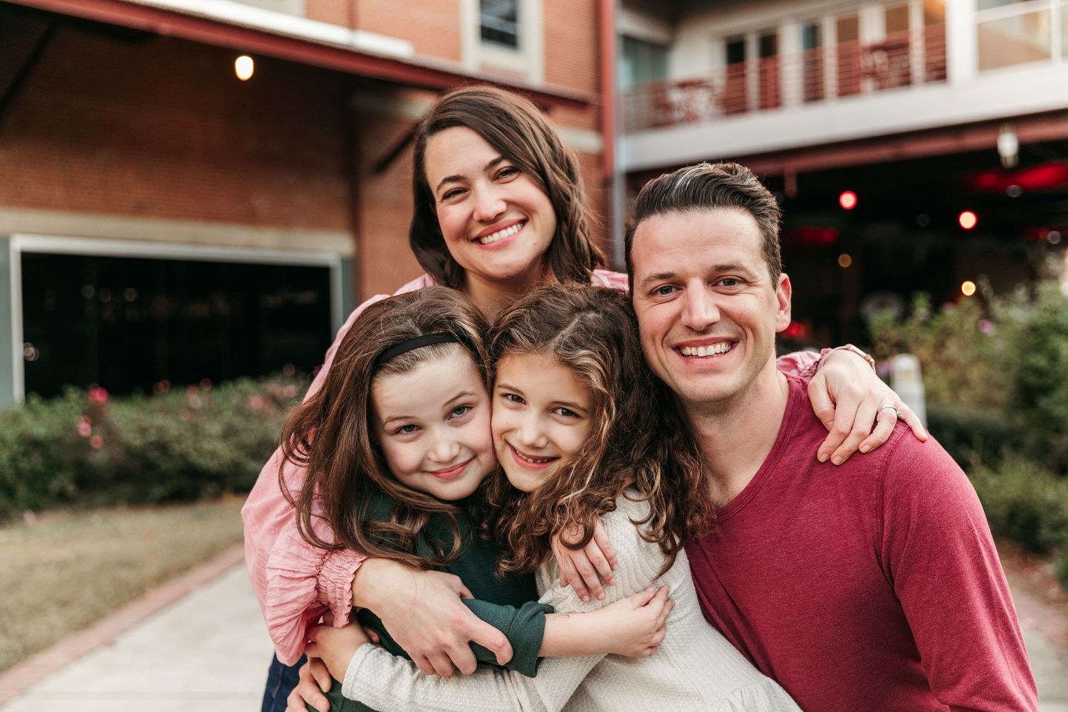 Family smiling and hugging while posing for a casual outdoor portrait.