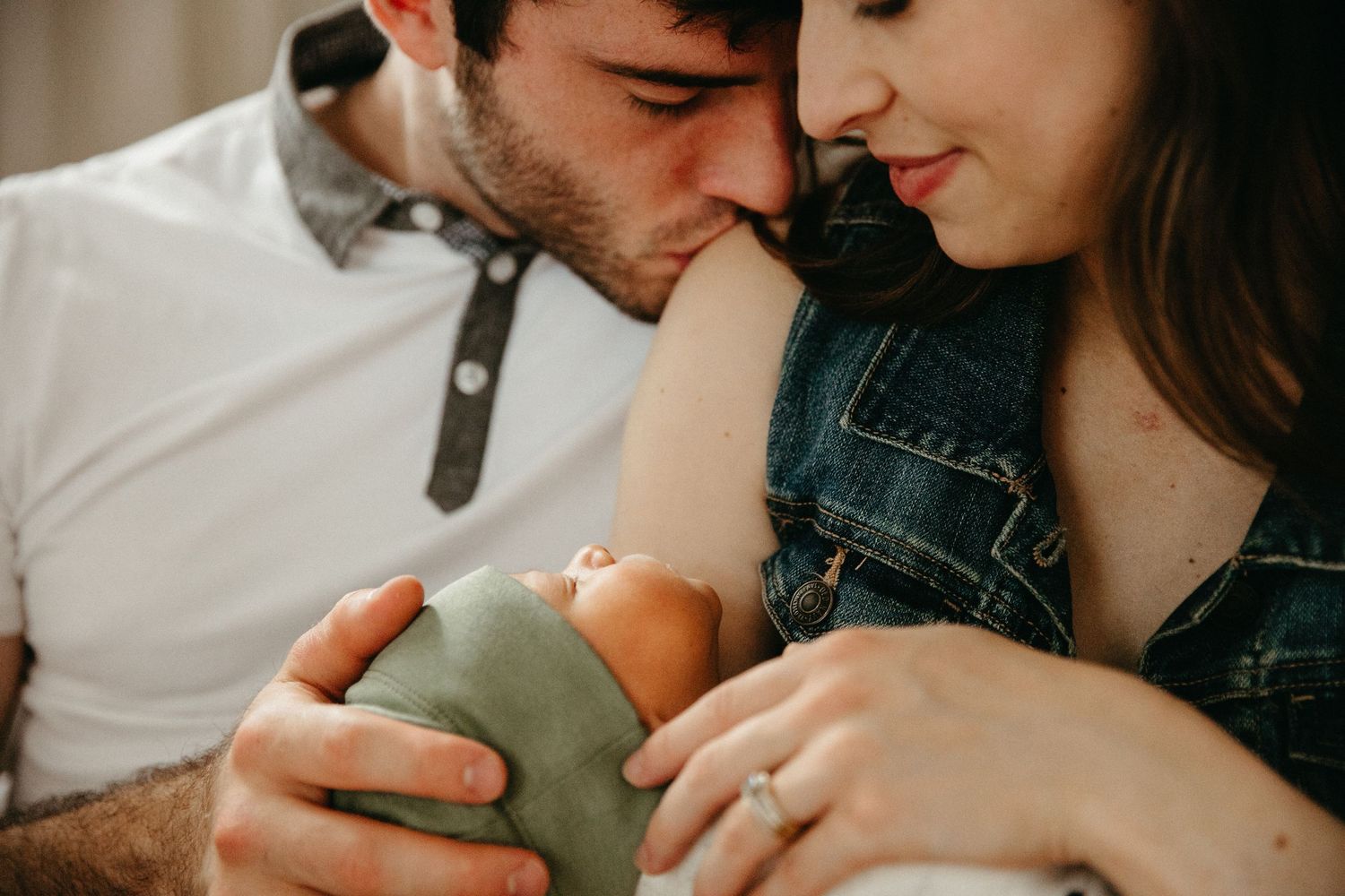 A couple shares an intimate moment while holding their sleeping newborn.