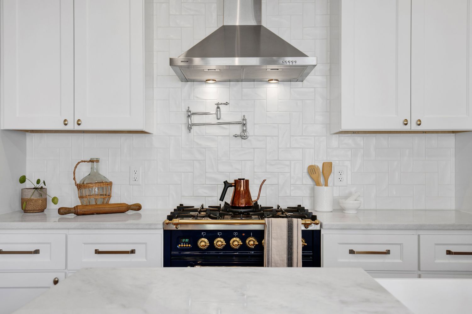 White kitchen with subway tile backsplash and stainless steel range hood.