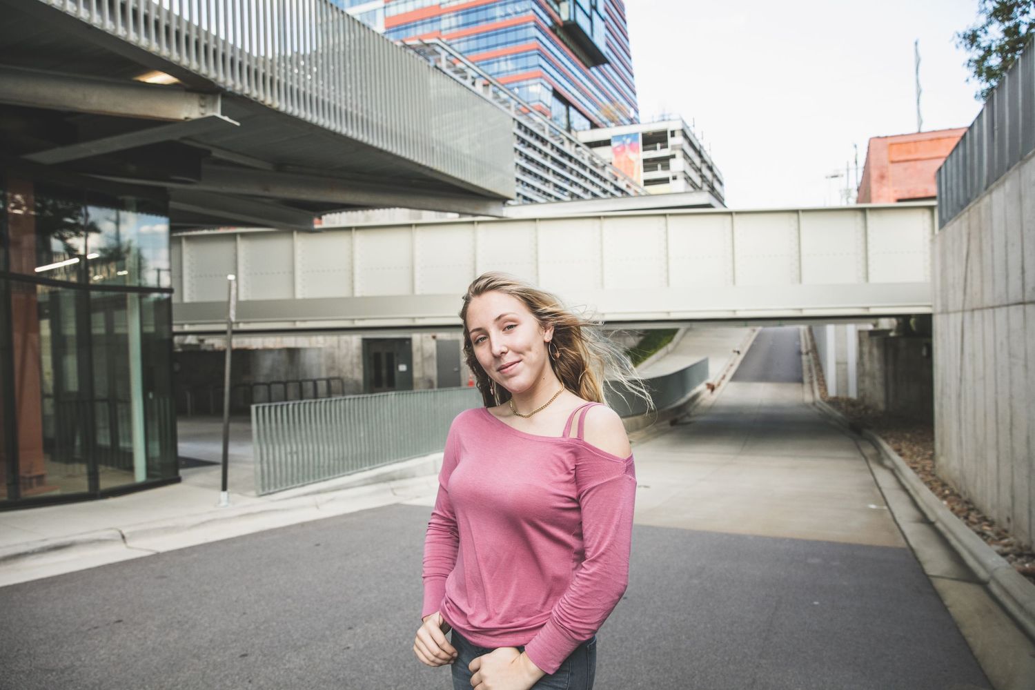 Street style portrait under modern architecture with pink off-shoulder sweater.