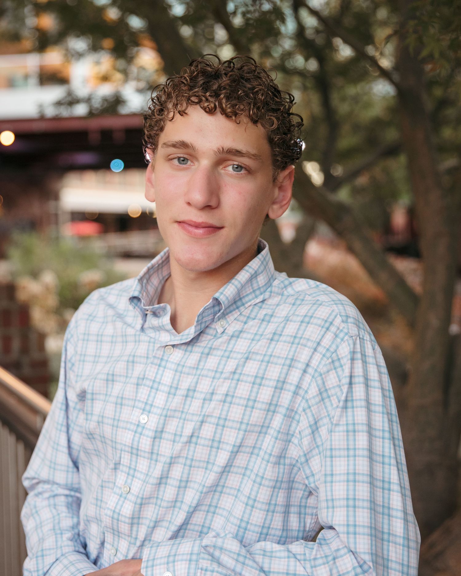Portrait of young person wearing light plaid button-down shirt outdoors.