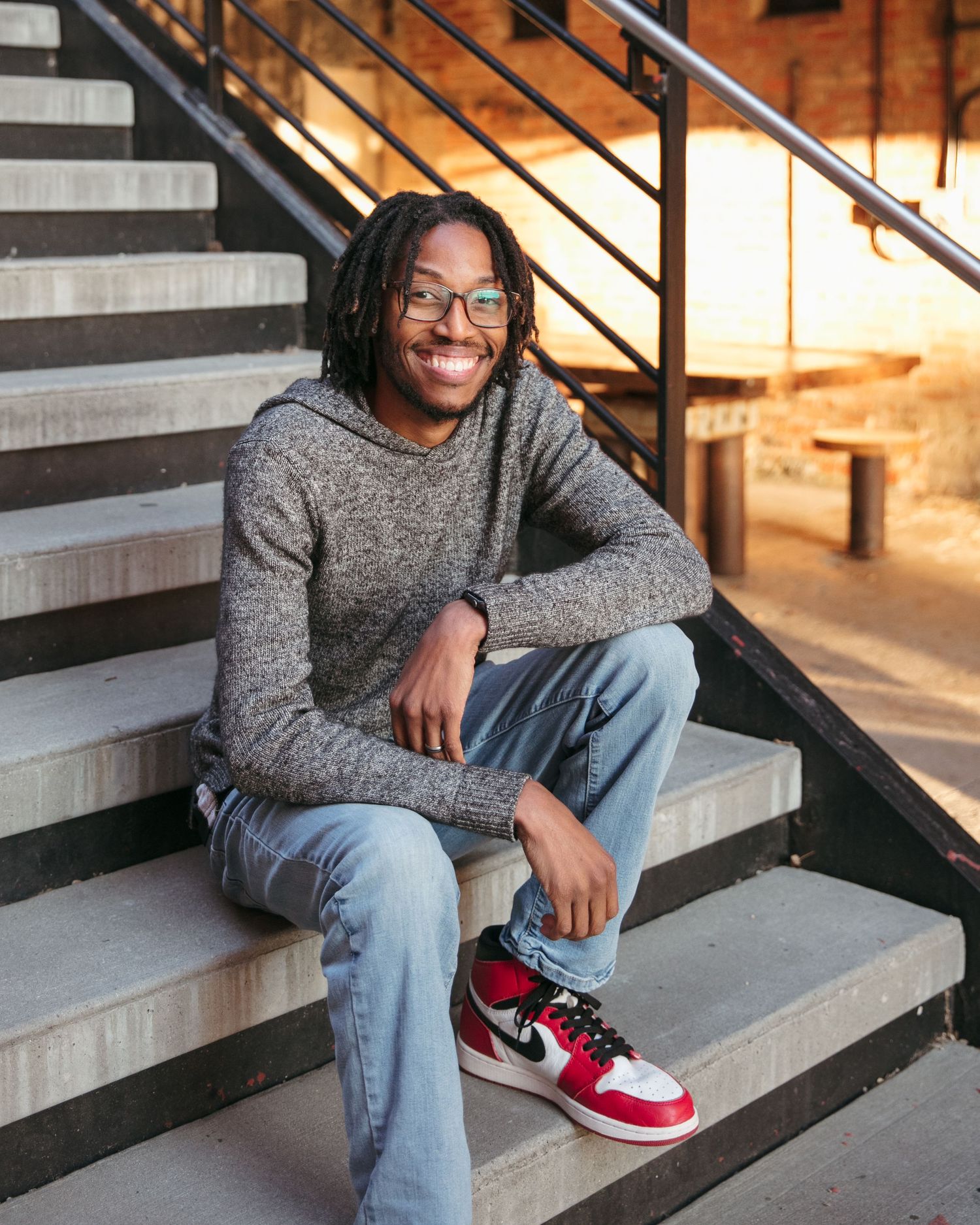 Person in gray sweater and jeans sitting on industrial staircase.
