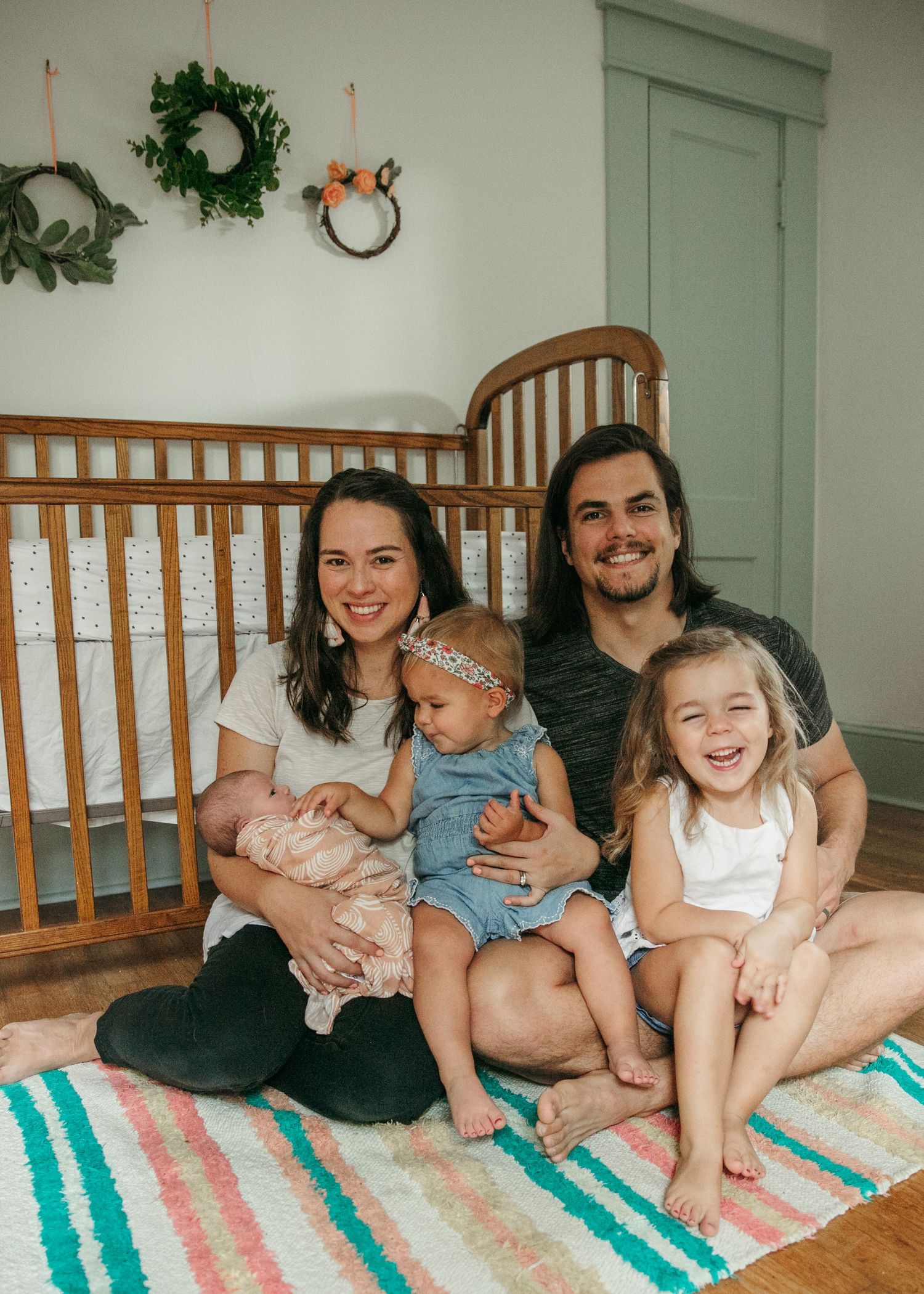Family relaxes together on striped rug during casual indoor photo session.