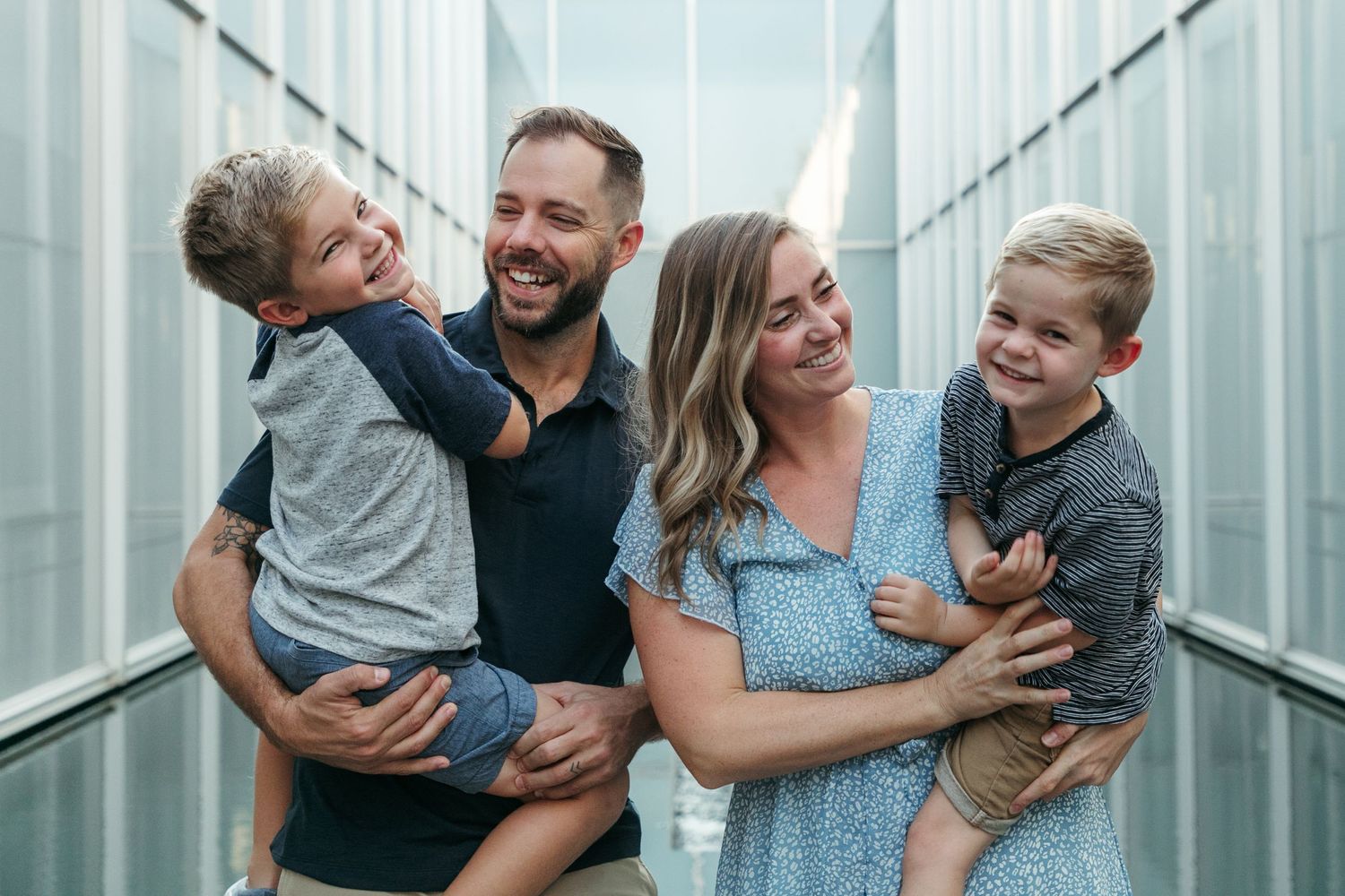 Family laughing together and hugging in an industrial hallway with metallic walls.