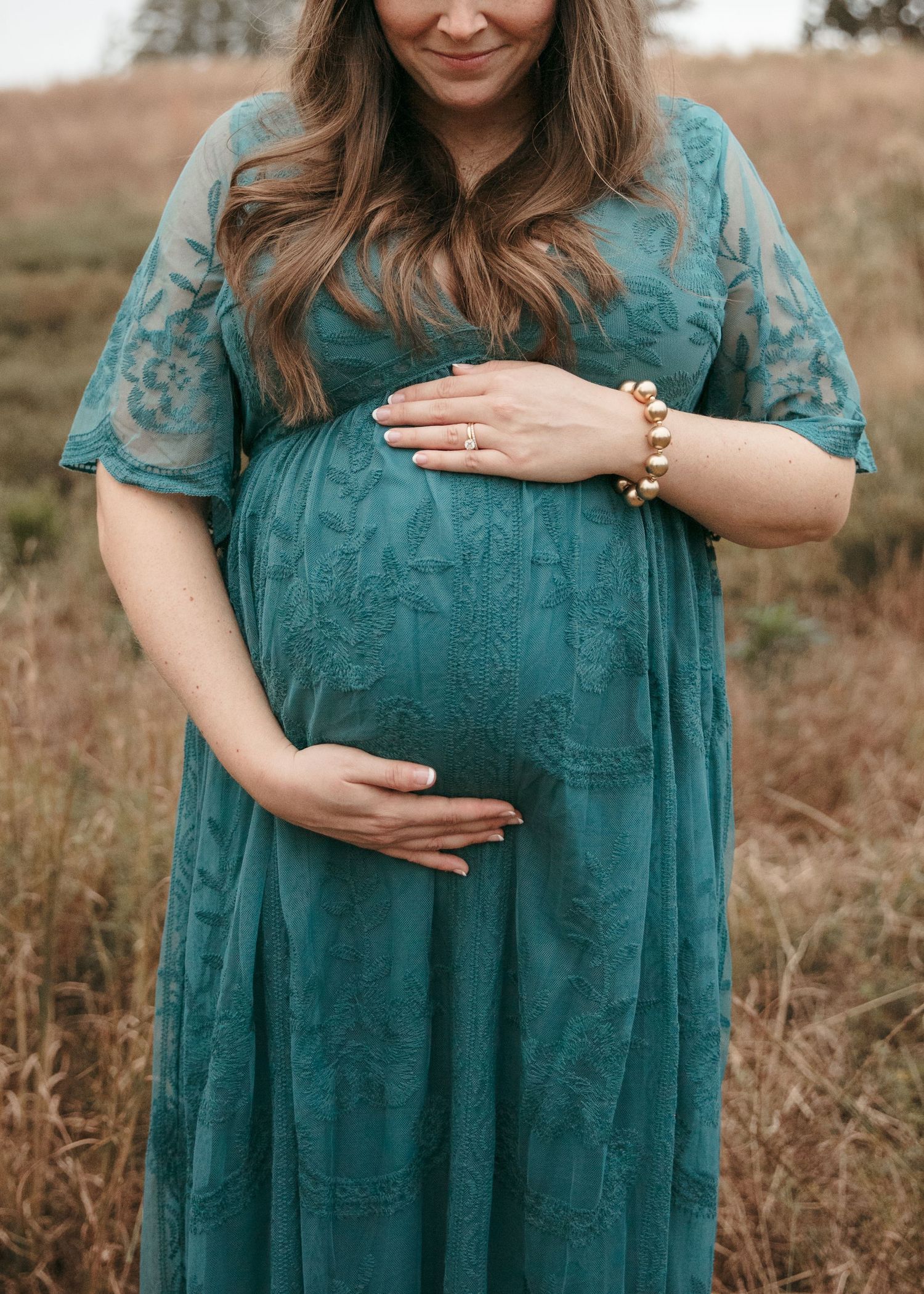 Person in teal lace dress showing baby bump in outdoor maternity photoshoot.