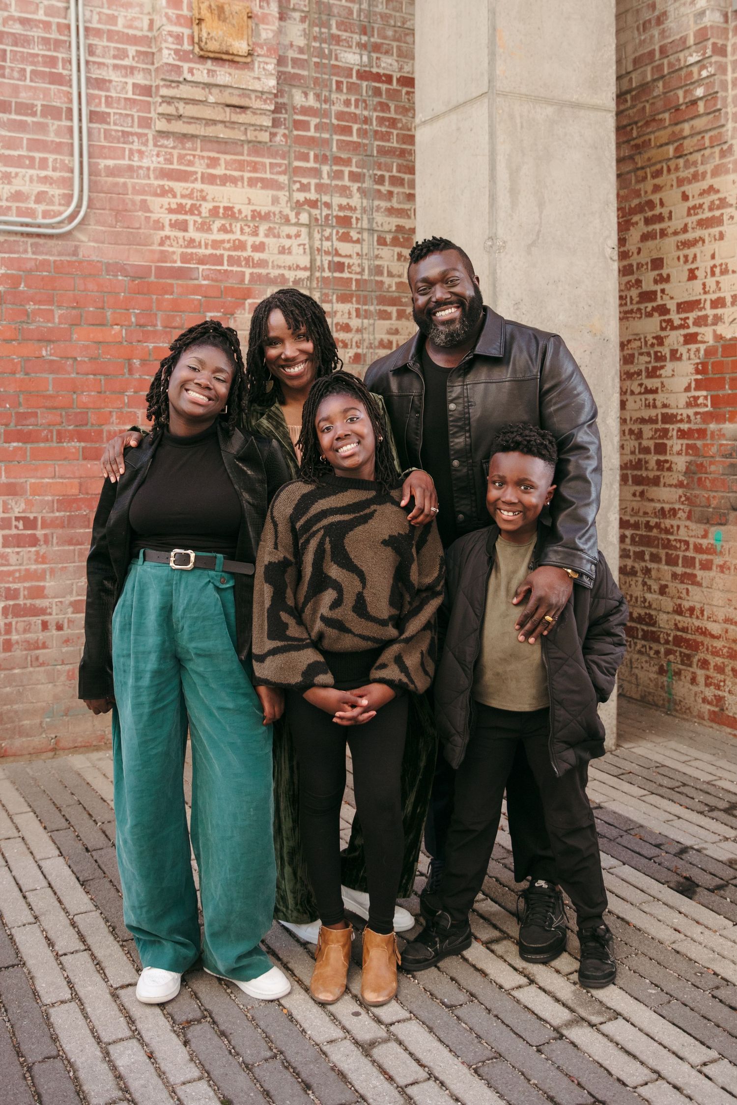Family portrait against rustic brick wall background in urban setting.