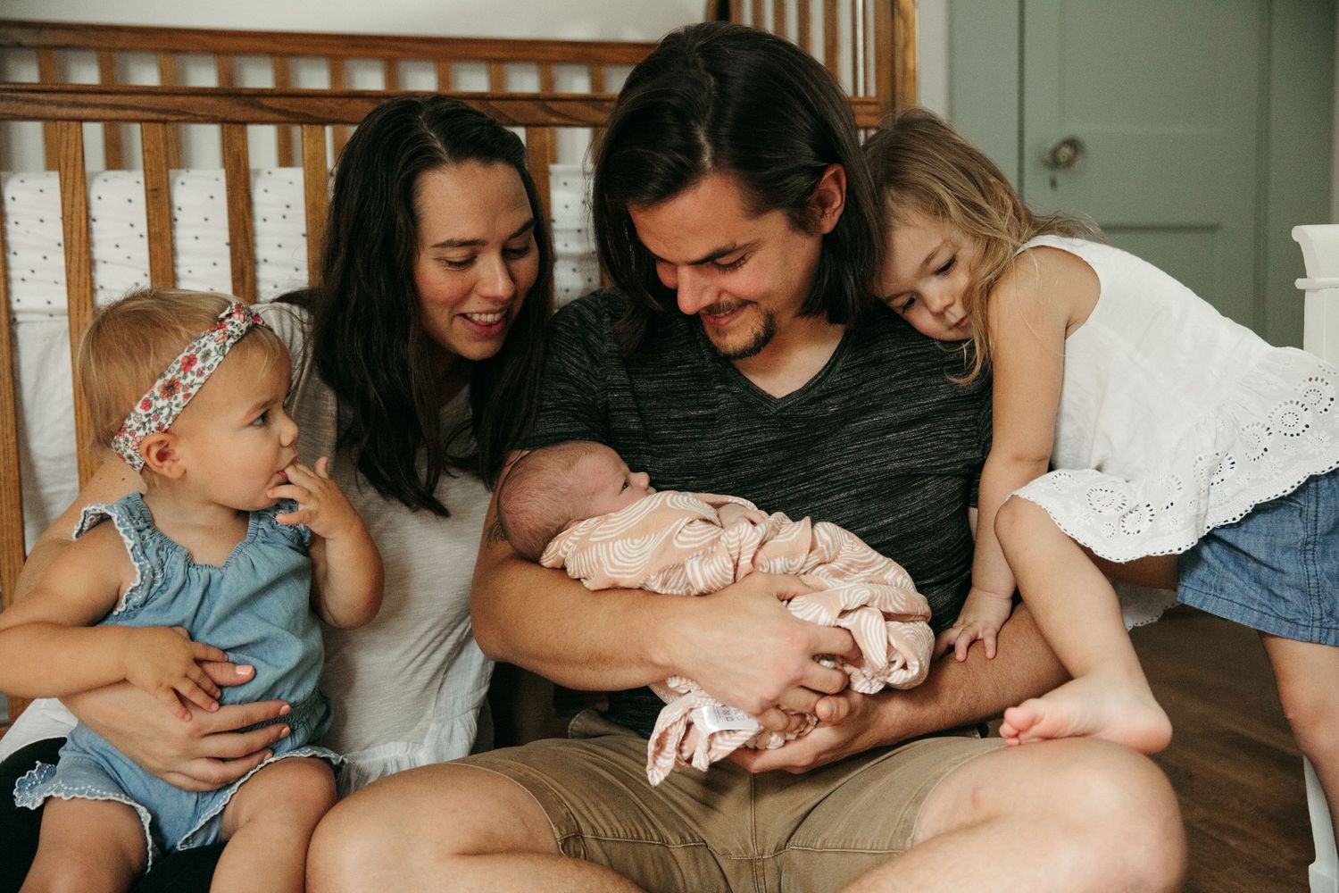 Family gathers on floor to welcome new baby sibling with tender expressions.