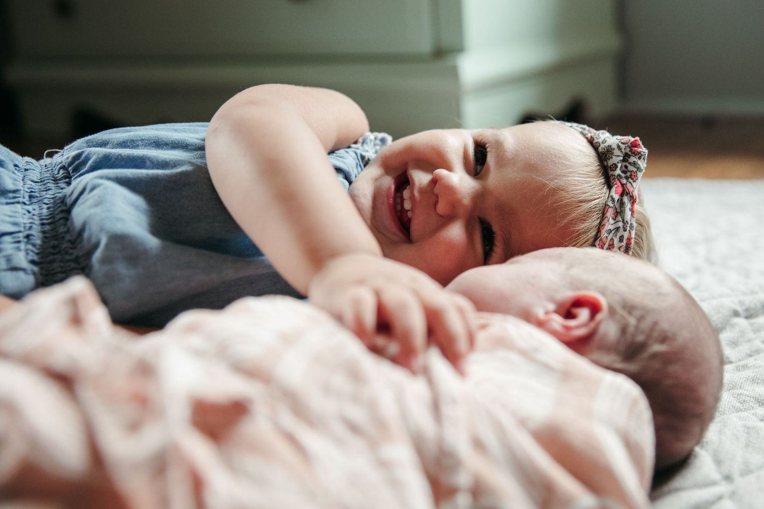 A baby lies on a soft white blanket while sleeping peacefully in natural light.