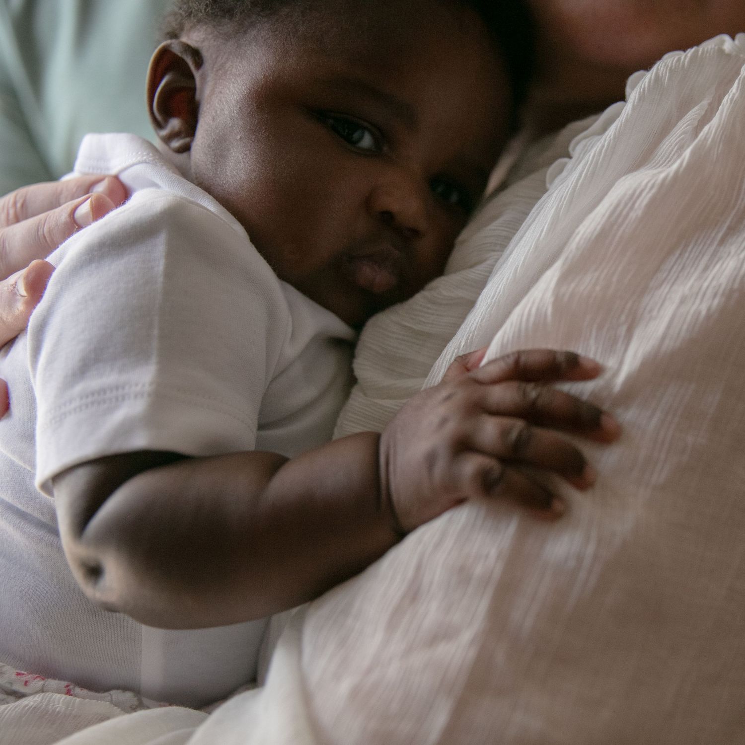 A series of four similar photos showing a sleeping baby in white clothing resting on light-colored bedding.