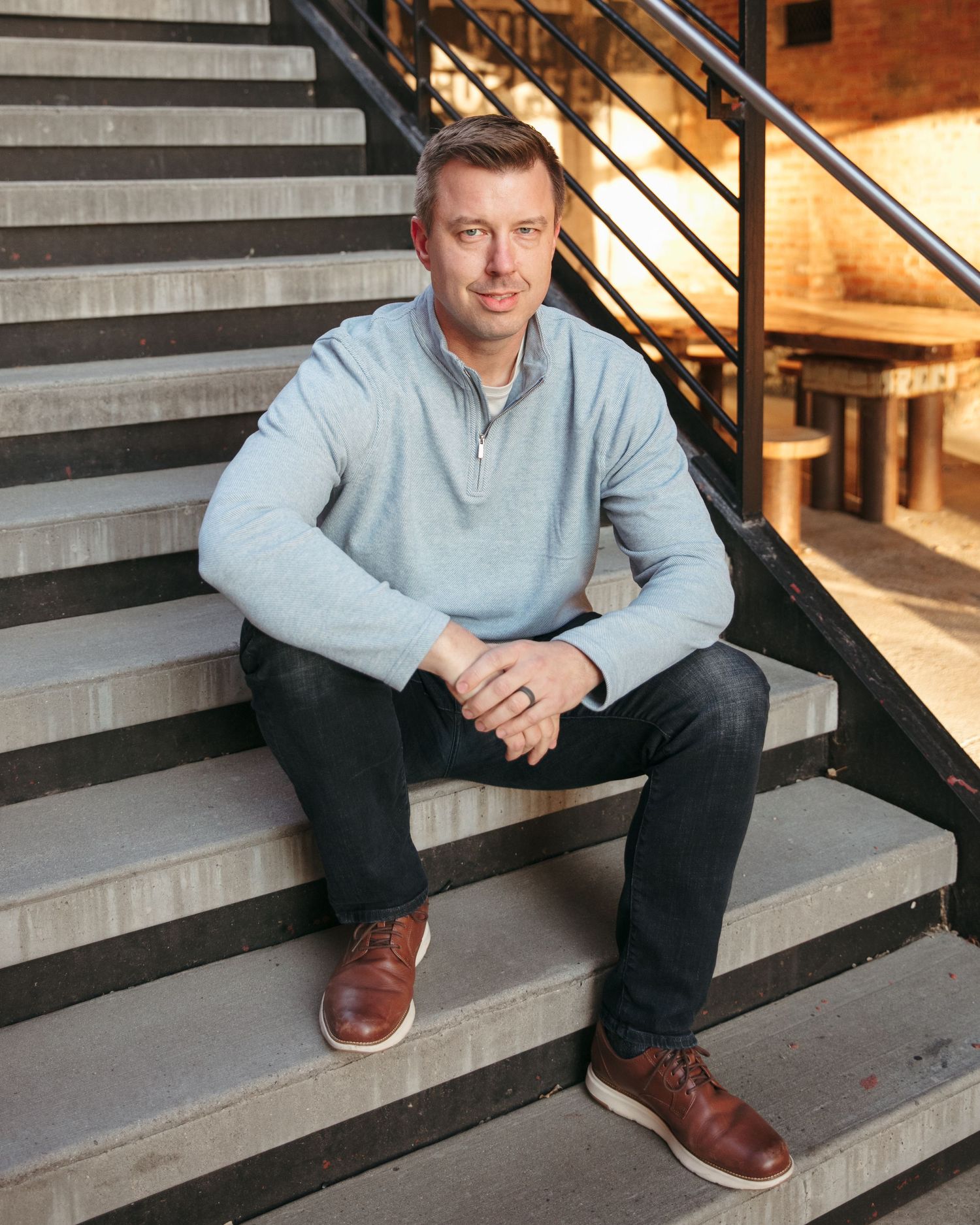 Person in light colored sweater sitting casually on gray stairs.