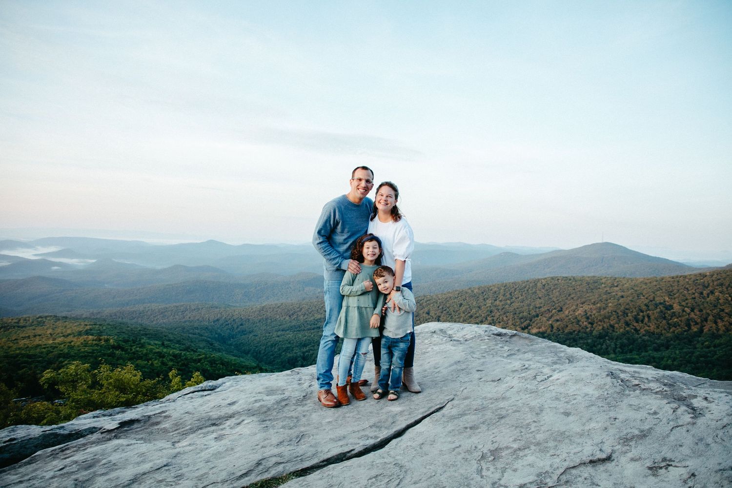 Couple standing close together on a mountain summit overlooking a vast wilderness landscape.