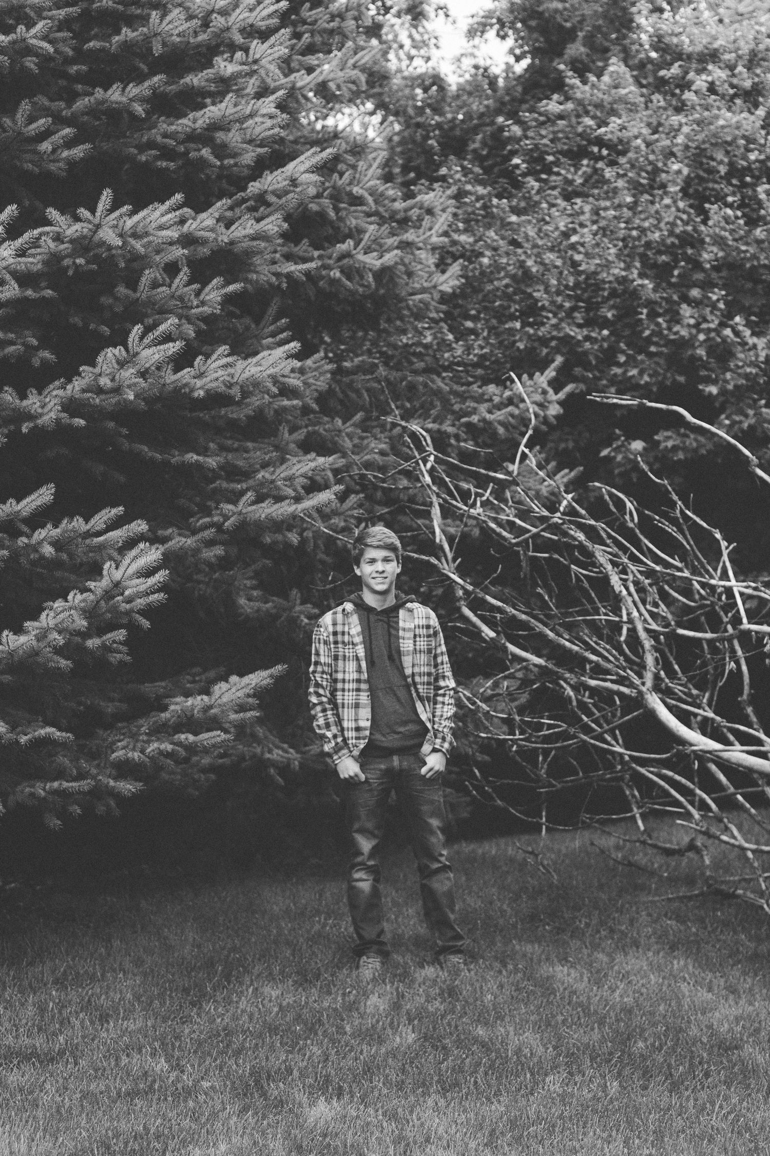 Black and white portrait in casual plaid against evergreen trees and branches.
