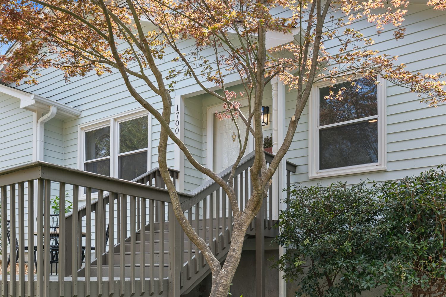 Gray siding home exterior with wooden deck stairs and colorful autumn tree in foreground.