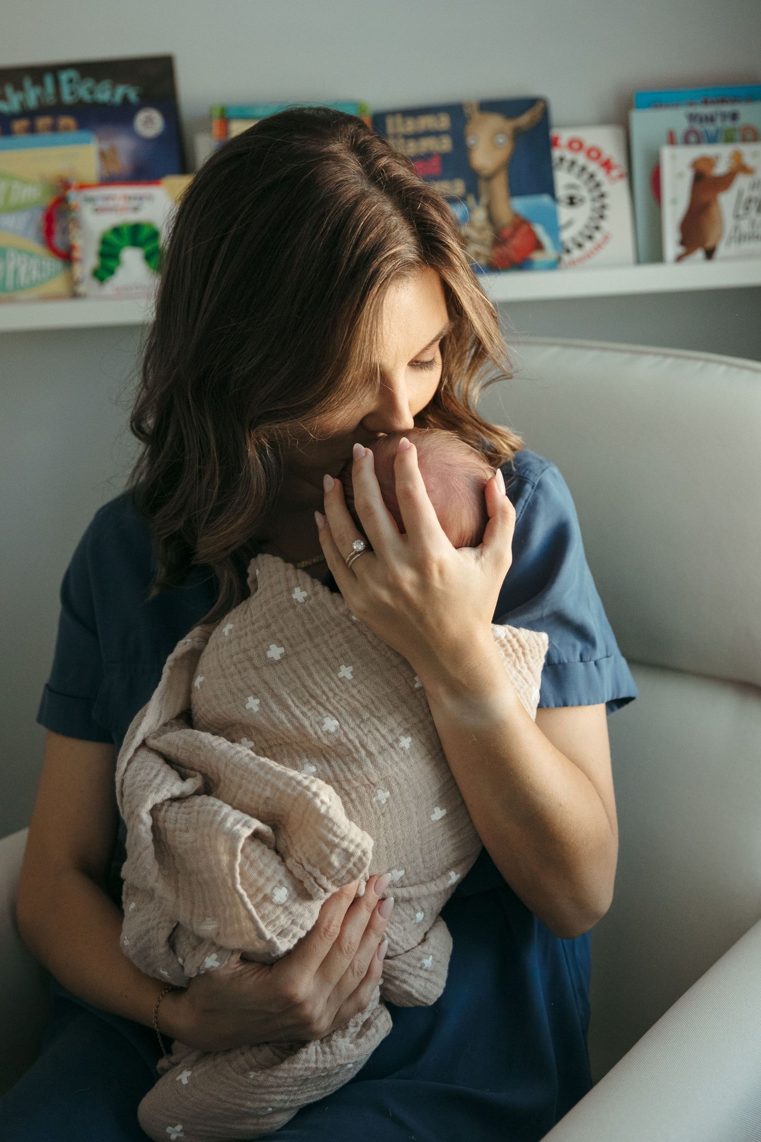 A nurturing moment in a cozy nursery with children's books displayed on shelves in the background.