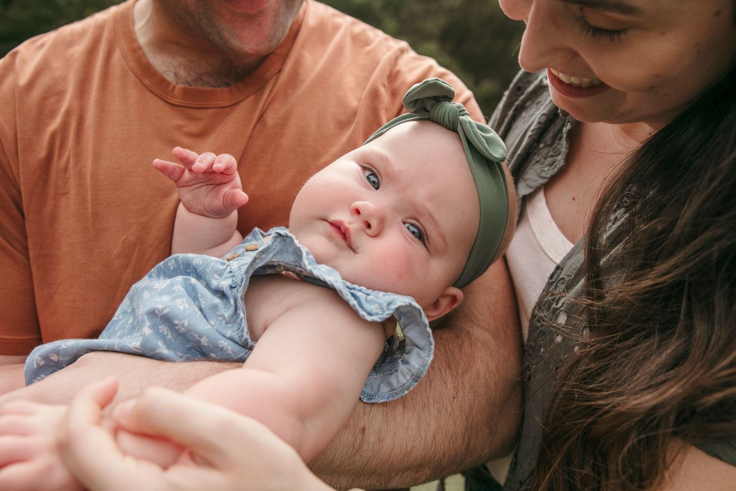 Close-up of an infant with curious expression being held by parents outdoors.