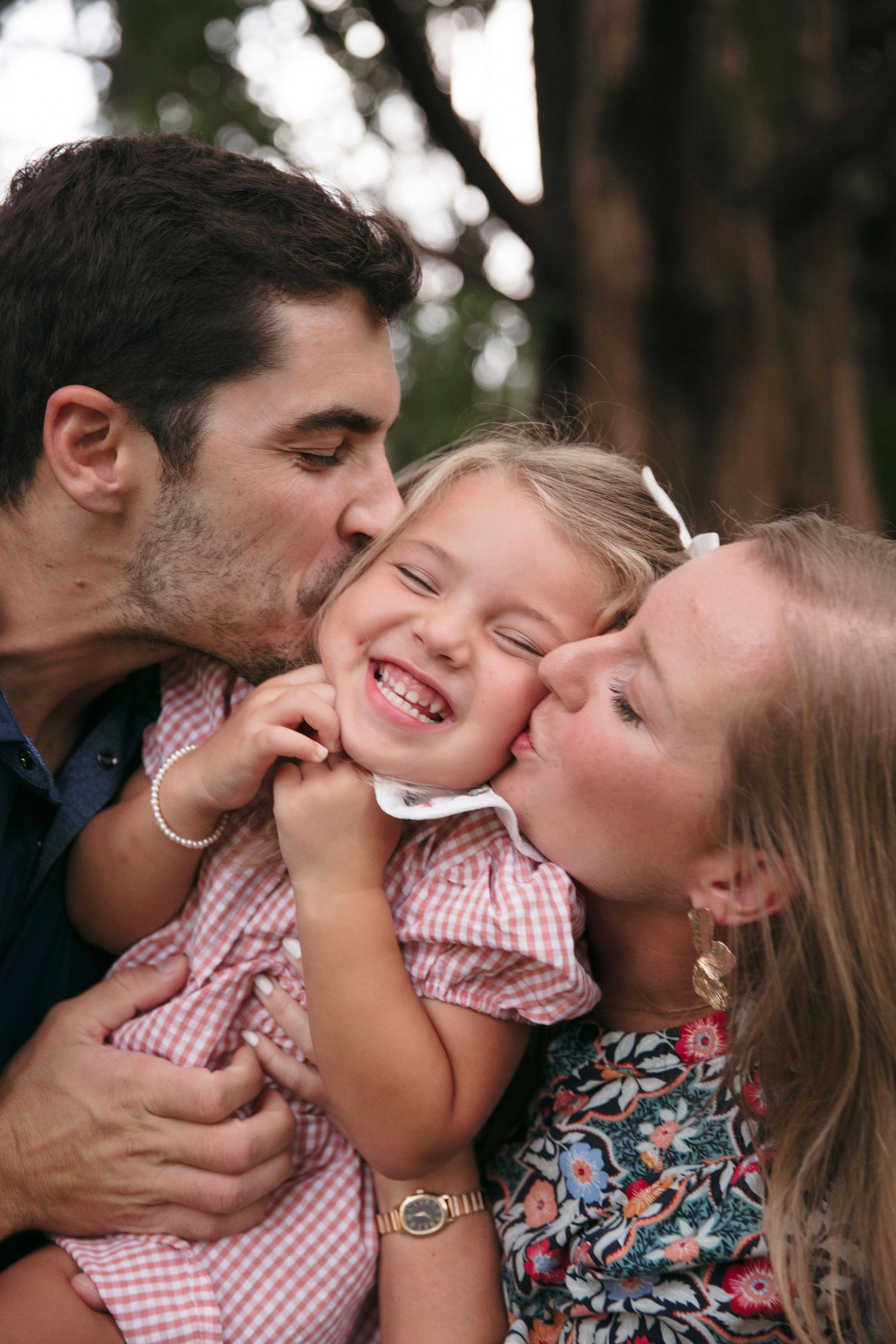 Sweet family moment with playful expressions and kisses in a natural outdoor setting.
