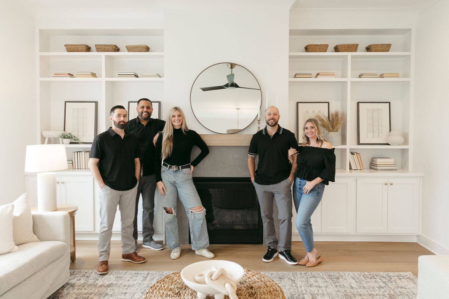 Group photo in front of a modern fireplace with built-in shelving and round mirror.