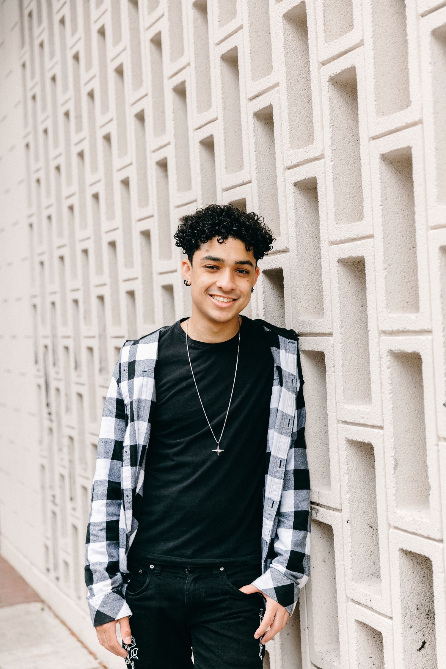 Person in casual black outfit posing against geometric white wall pattern.