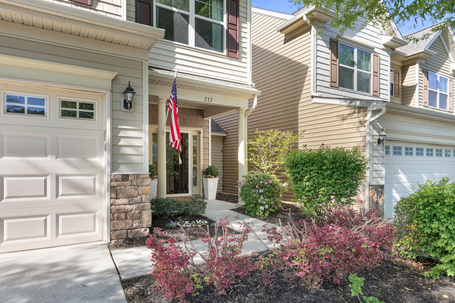 Charming two-story townhome with stone accents, white garage door, and American flag at inviting front entrance.