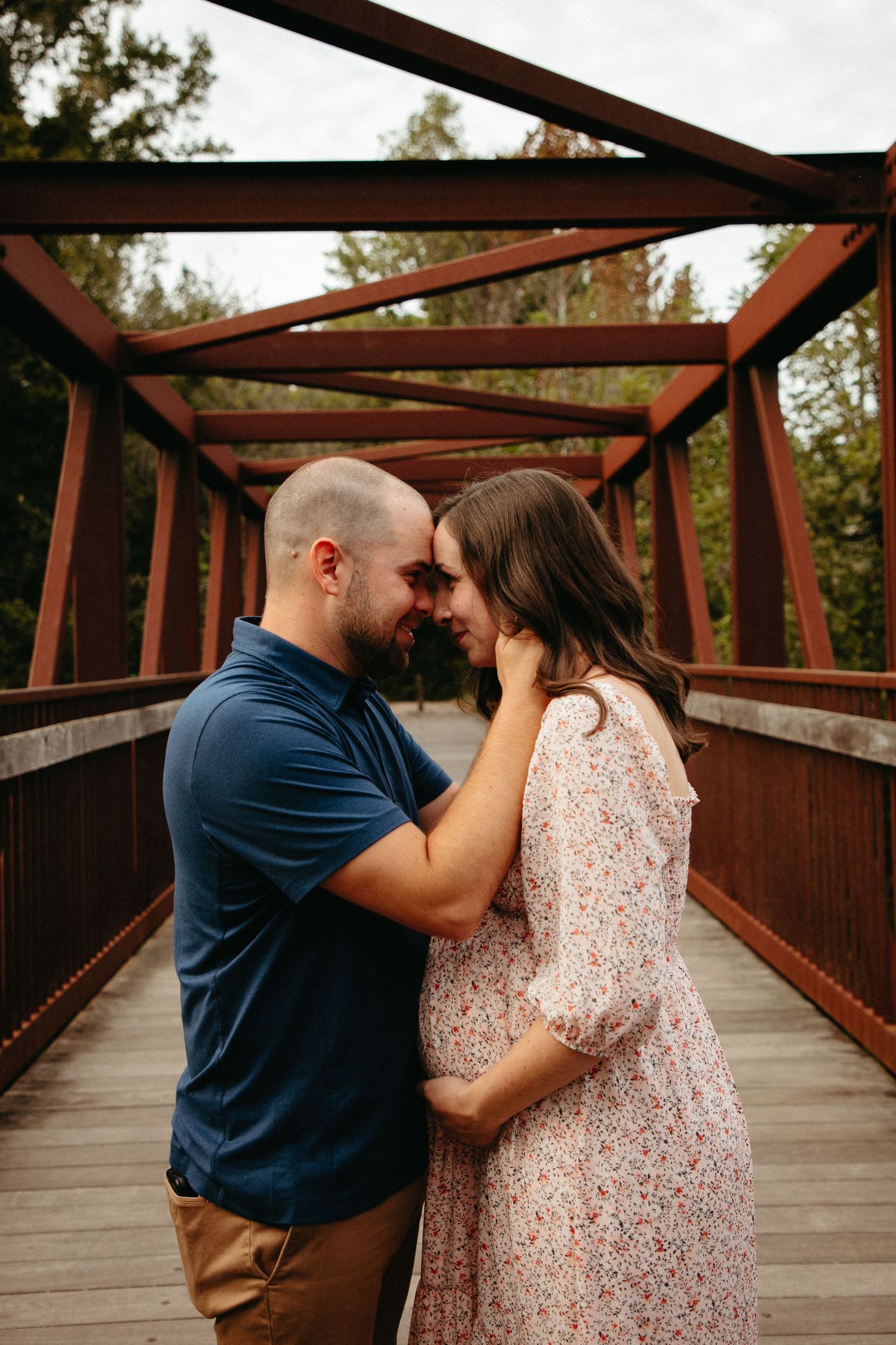 An intimate moment between a couple on a rustic wooden bridge with metal beams overhead.