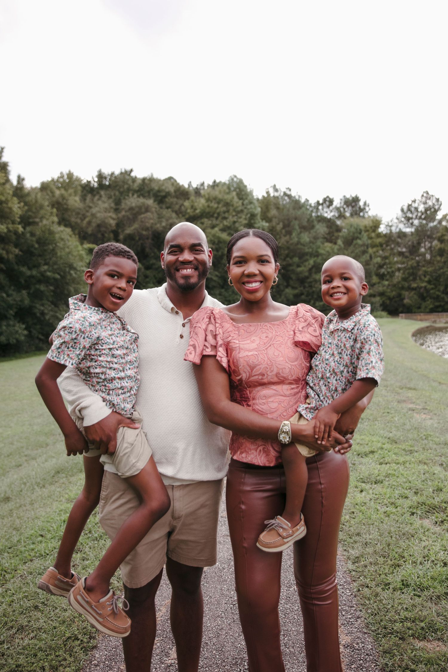 Happy family of four poses together on a path surrounded by trees.