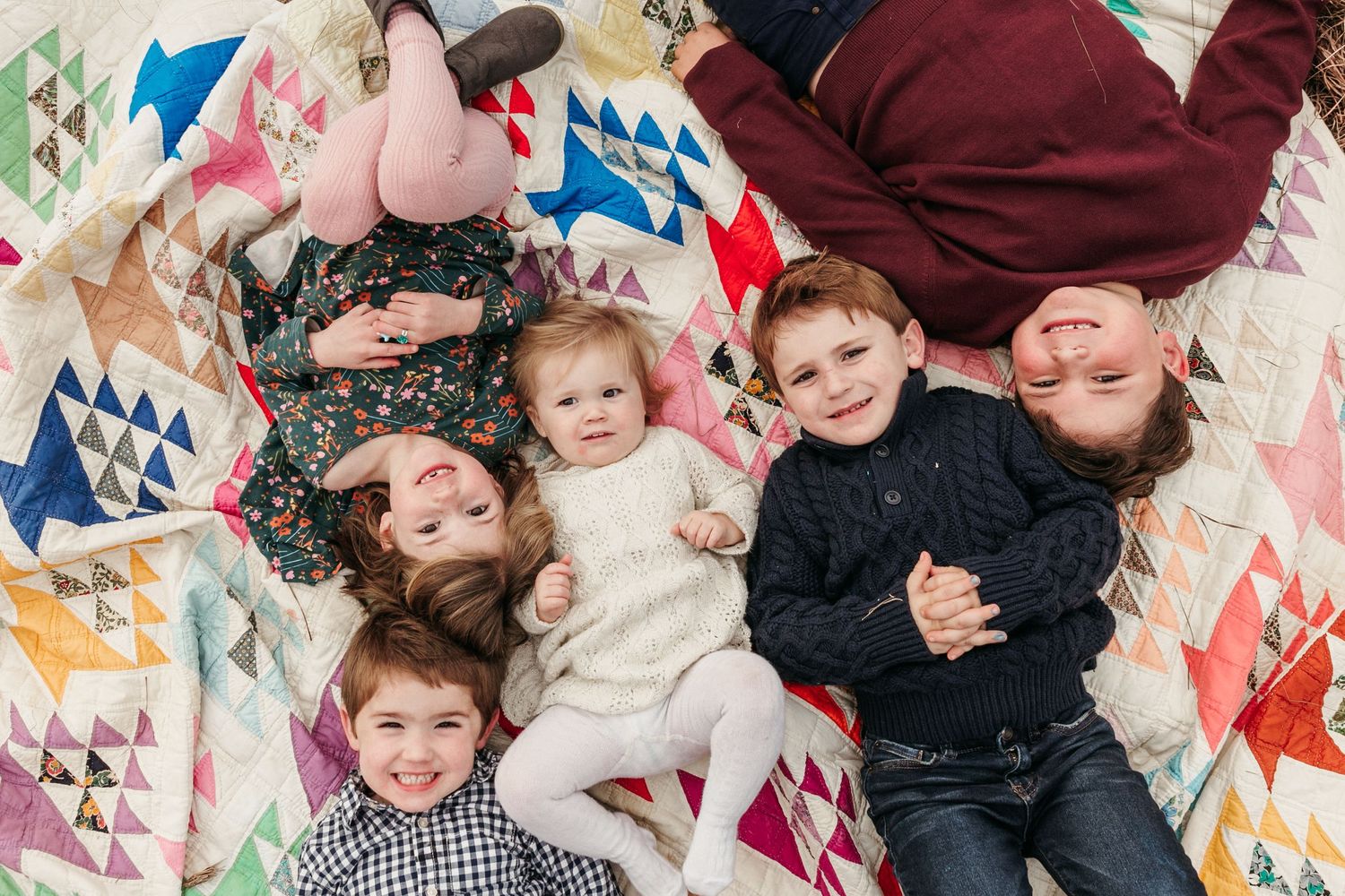 Group lying on colorful geometric patterned quilt looking up at camera.