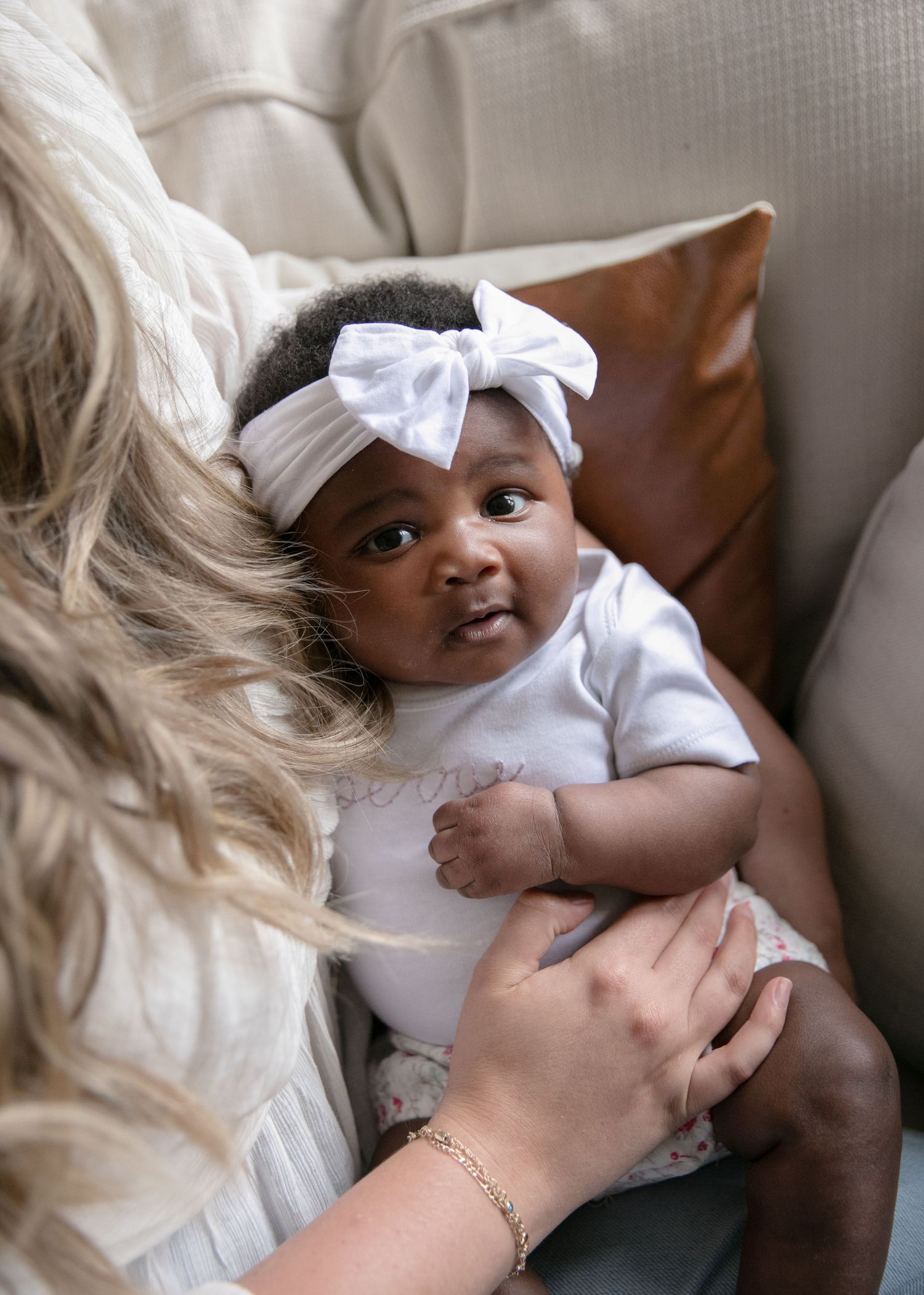 Baby wearing white bow headband rests against brown leather couch cushion.