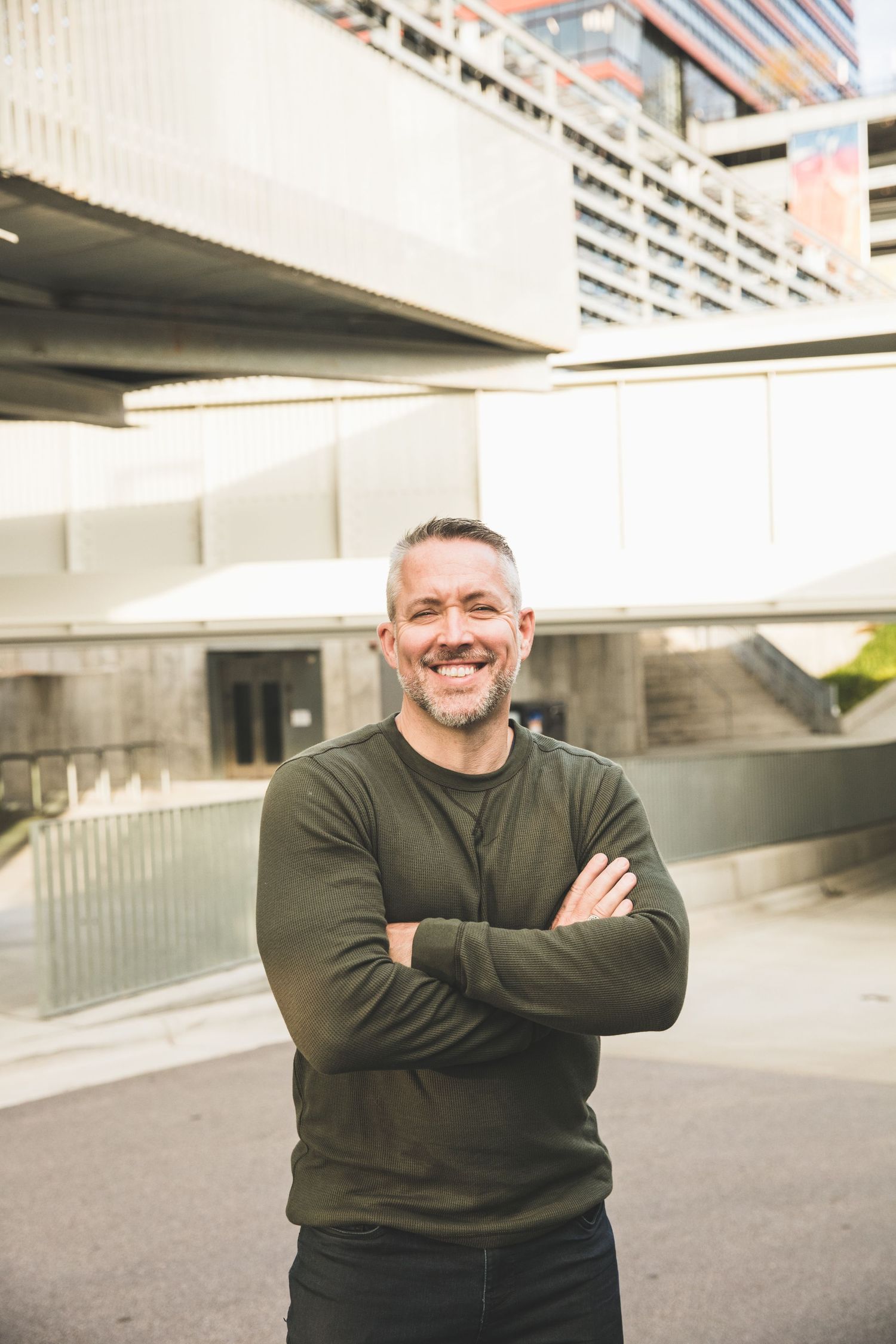 Casual portrait against modern architectural background with glass and concrete elements.