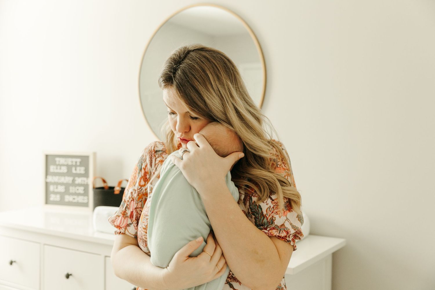 Intimate nursery moment captured in mirror reflection with floral dress.