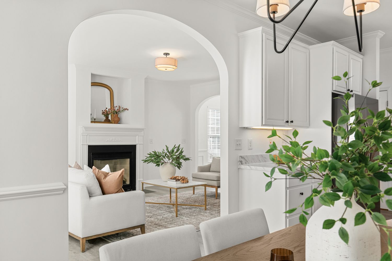 Elegant white living room with arched doorway, fireplace, and neutral furnishings visible from bright dining area.