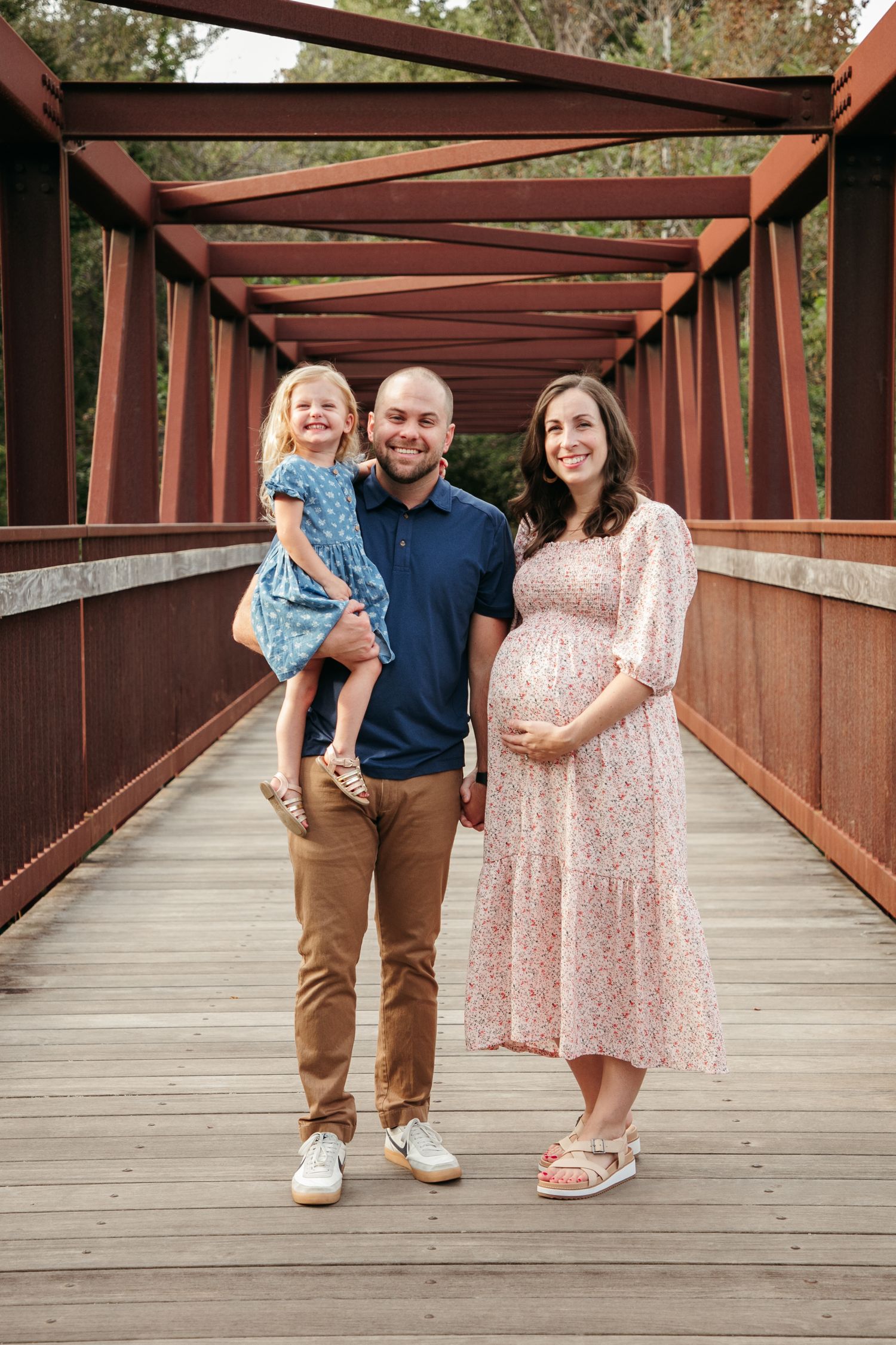 Family in coordinated outfits posing on a covered wooden bridge.