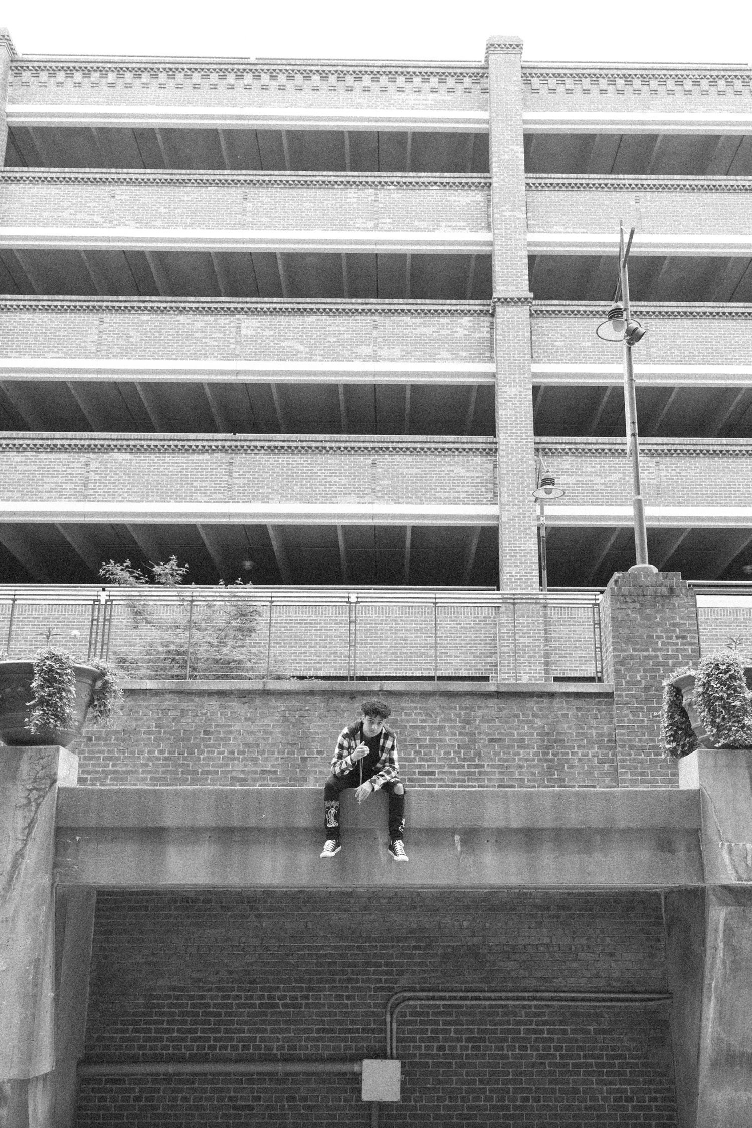 Black and white architectural photo of person sitting on ledge of multi-level parking structure.
