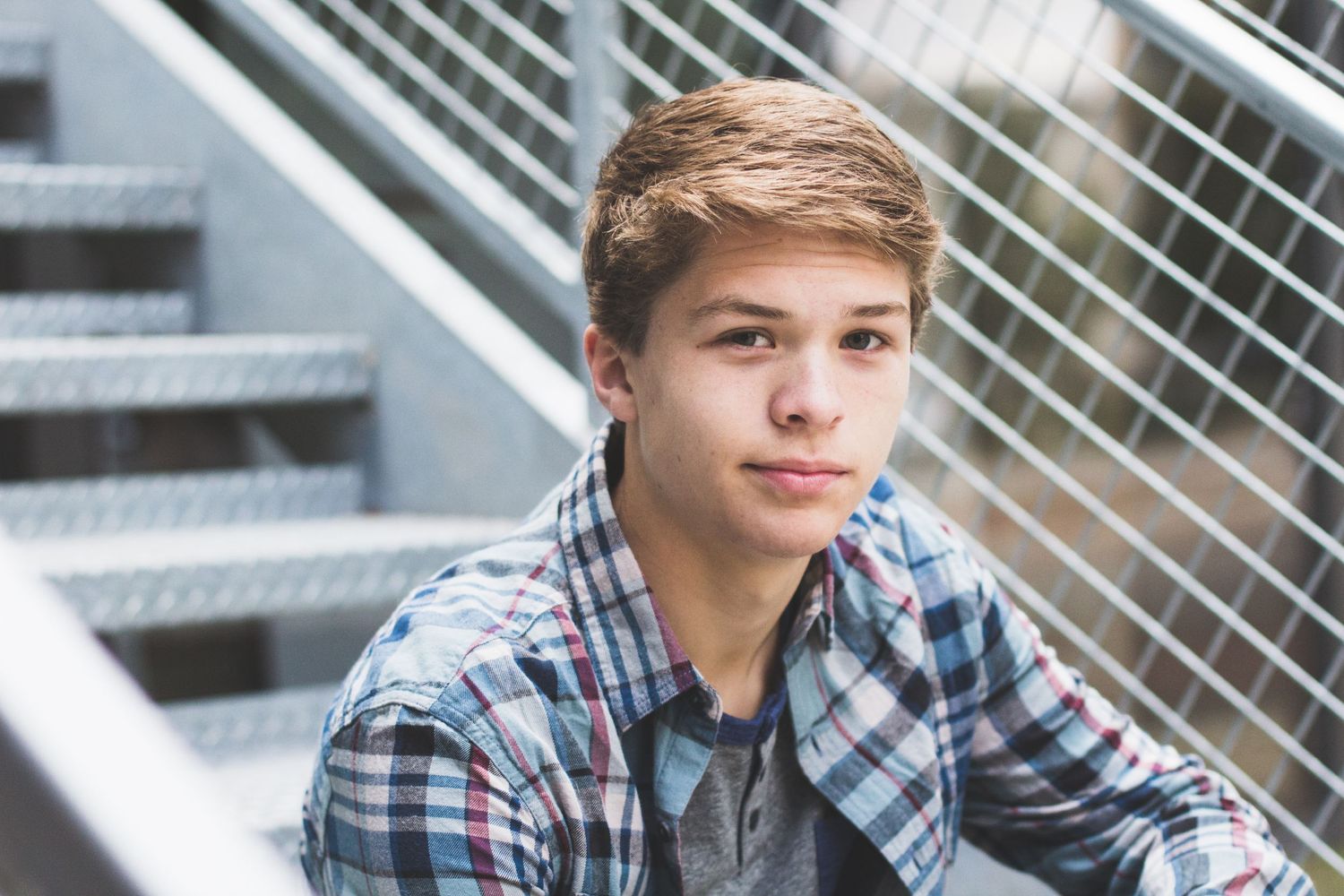 A portrait of someone in a plaid shirt against metal stairs and railings.