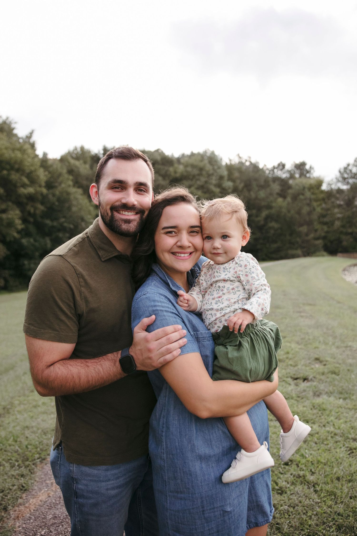 A small family shares a warm embrace while posing outdoors in casual attire.