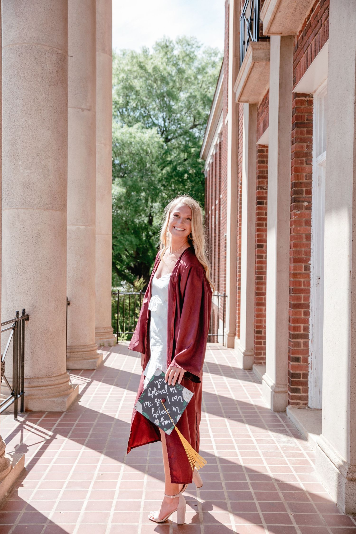 Graduate walks through columned architecture in burgundy graduation attire.