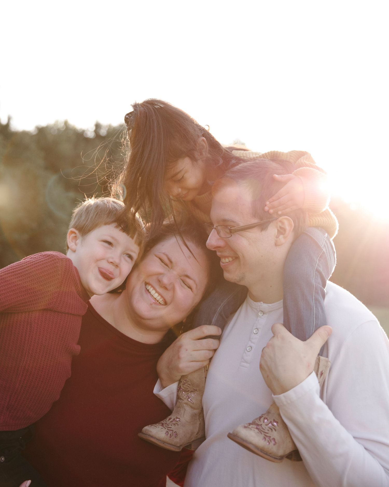 Family shares joyful embrace while laughing together in golden sunset light.
