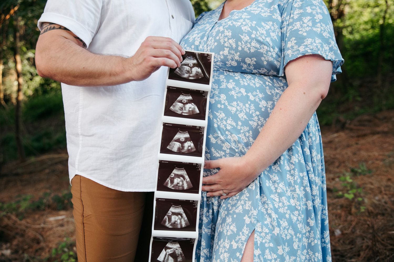 Couple holding ultrasound photos outdoors during pregnancy announcement photoshoot.