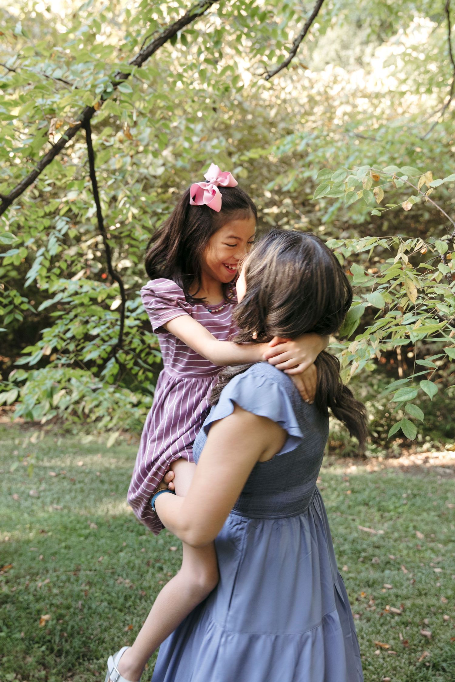 Parent and child sharing joyful embrace outdoors among trees and greenery.