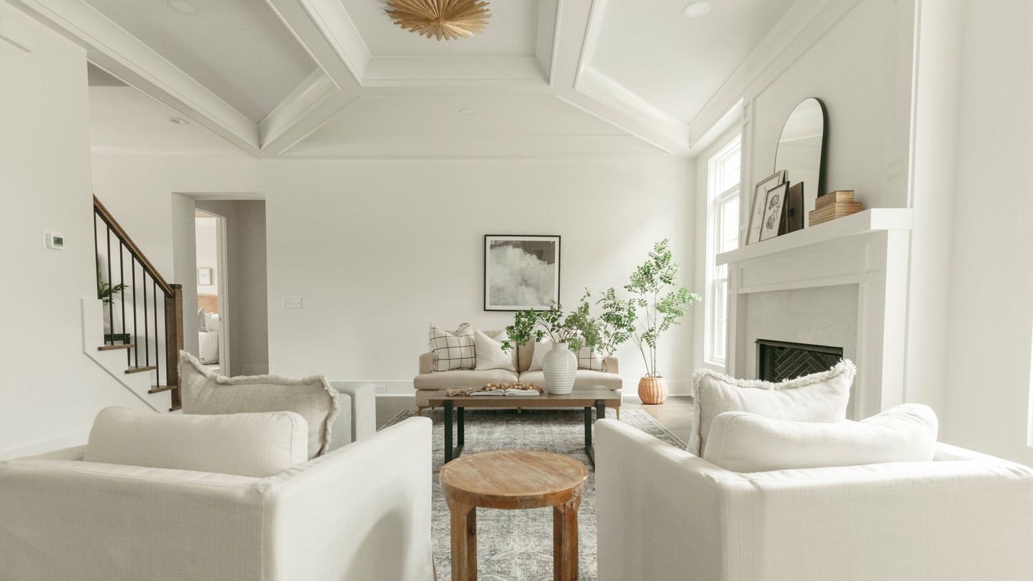Vaulted ceiling living room with white furniture, wooden coffee table and staircase view.